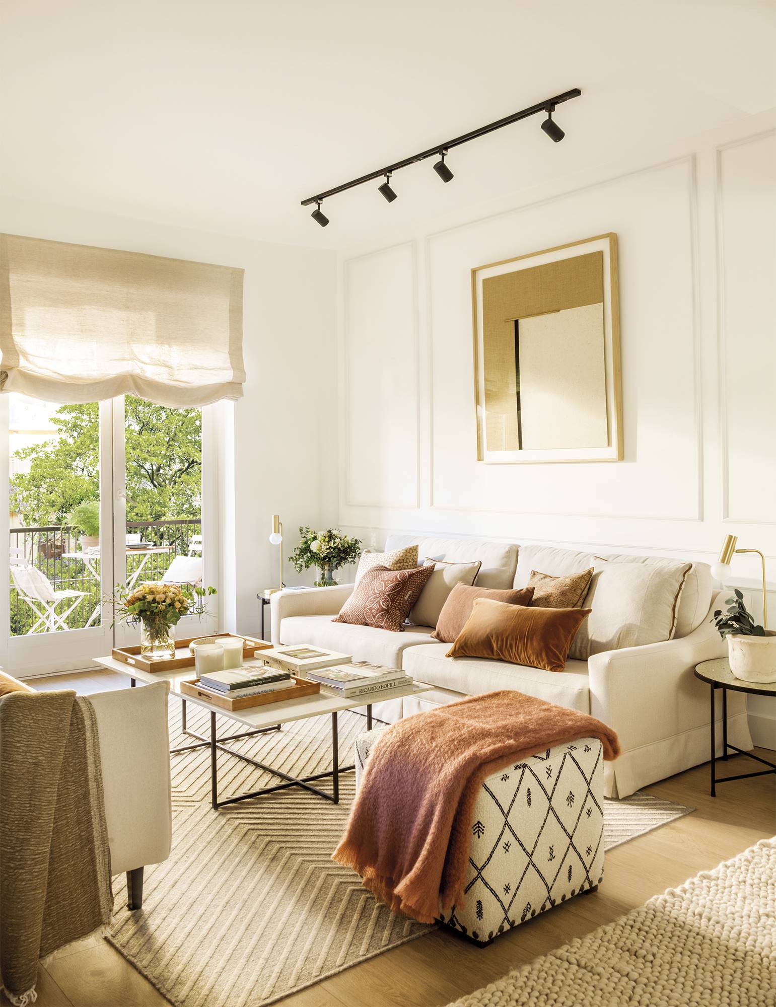 Salón moderno con sofás y puf en color crema, y cojines y plaid en tonos tierra. 