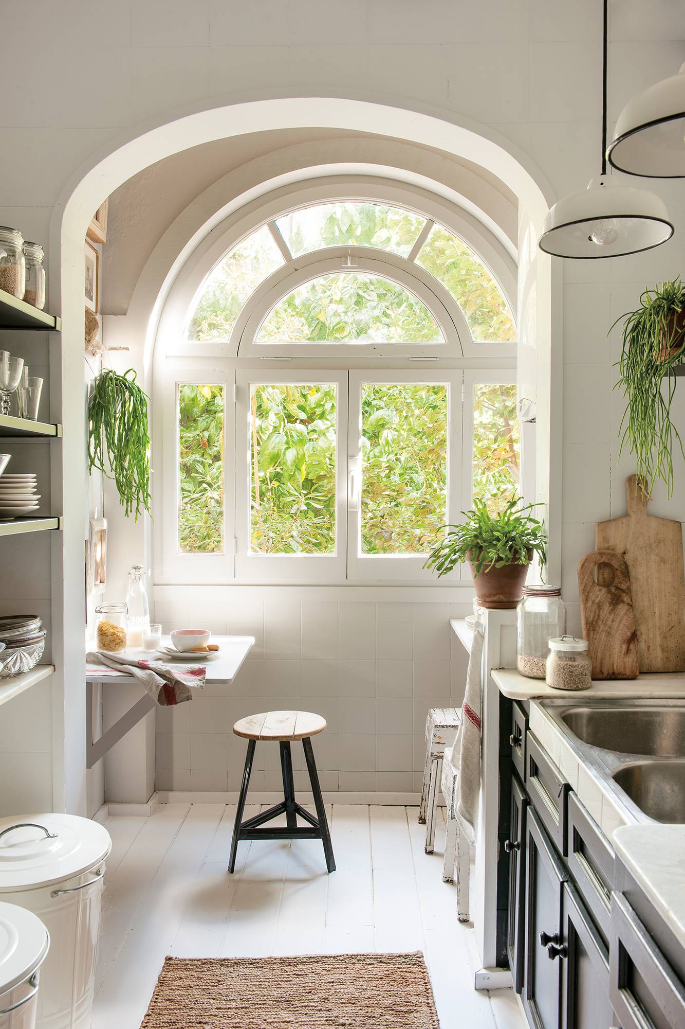 Cocina blanca con gran ventanal en forma de arco y muebles de cocina en negro.