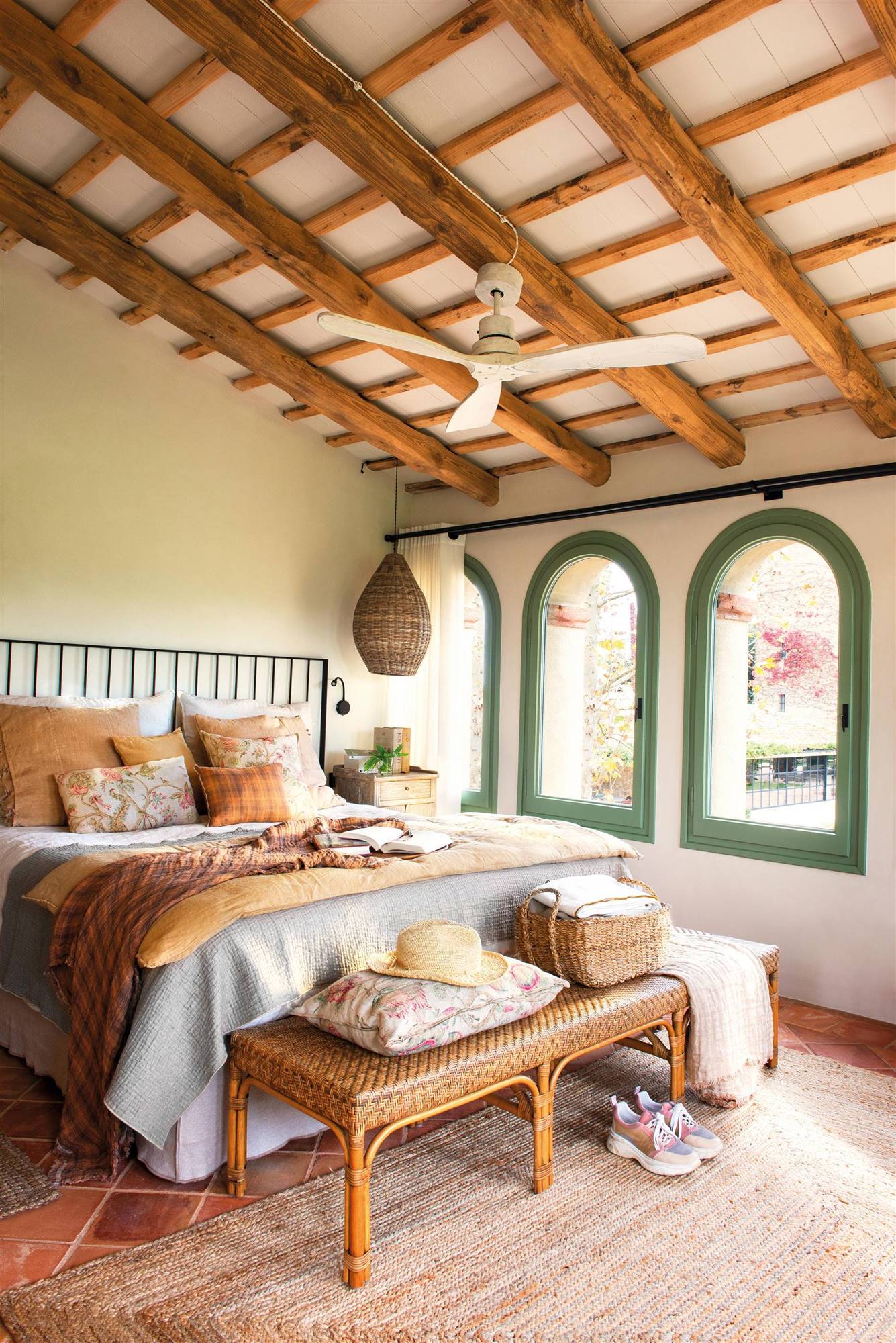 Dormitorio rústico con techos con vigas, cabecero de hierro y adornos en fibra natural. 