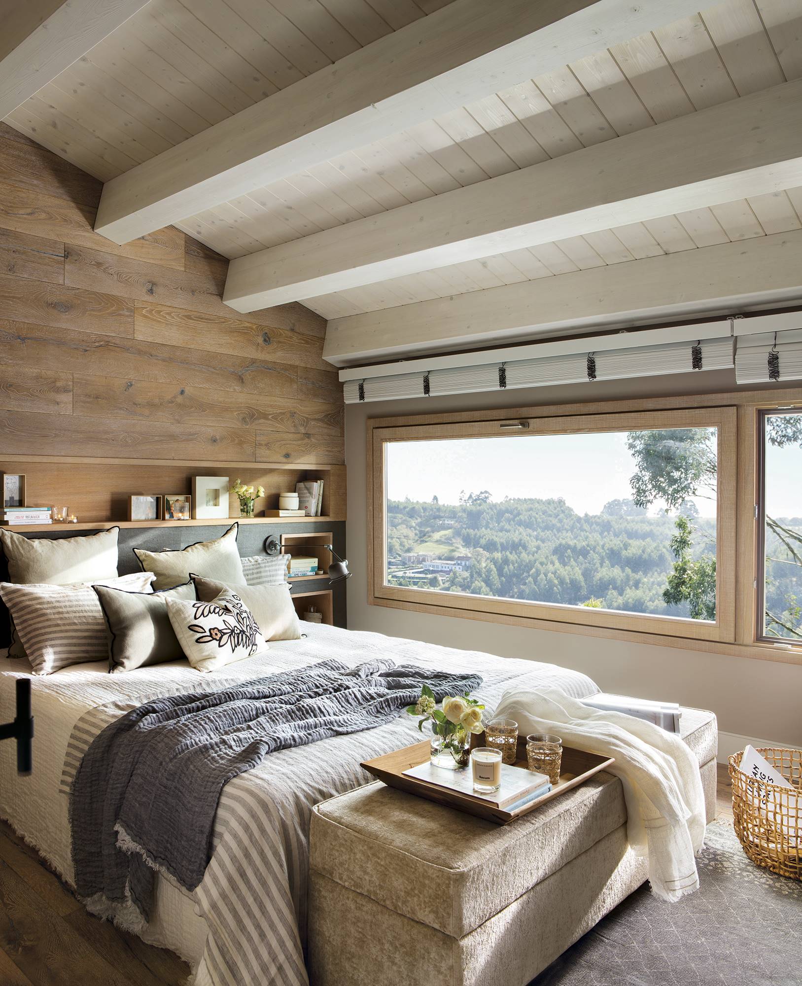 Dormitorio con cabecero de madera de roble, grandes ventanales y banco tapizado a los pies de la cama.
