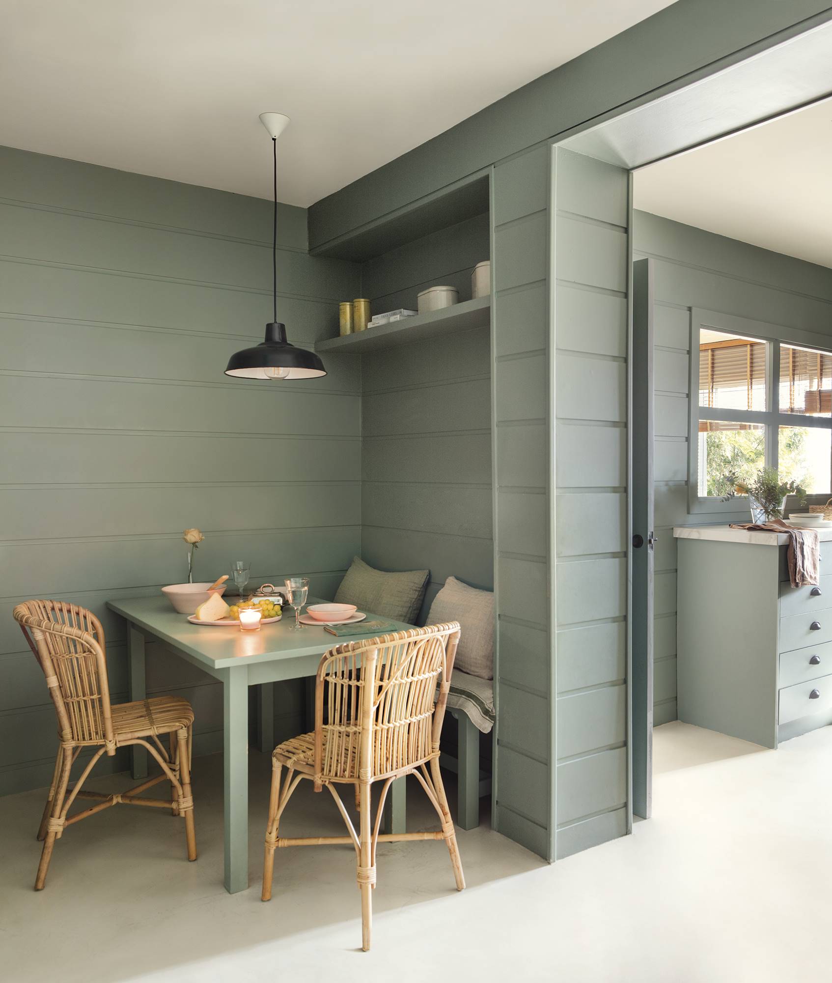 Office en la cocina pintado de color verde con mesa, banco y sillas de fibra natural.