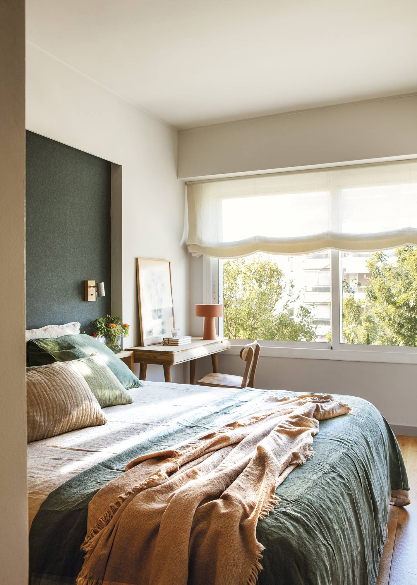 Dormitorio con cabecero decorado con papel pintado azul oscuro, textiles verdes y escritorio de madera.