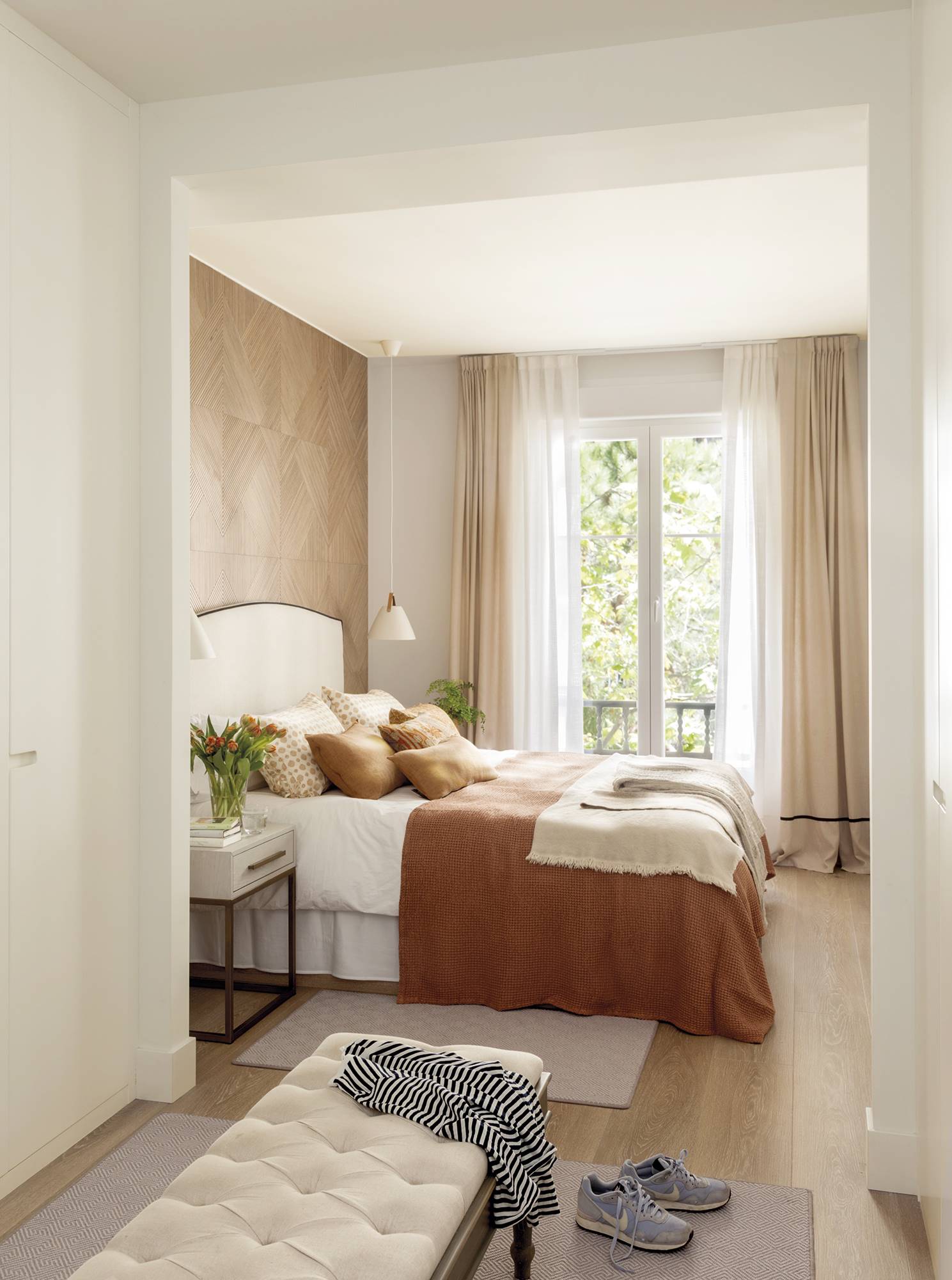 Dormitorio acogedor y clásico con vestidor, puf y gran cabecero de madera. 