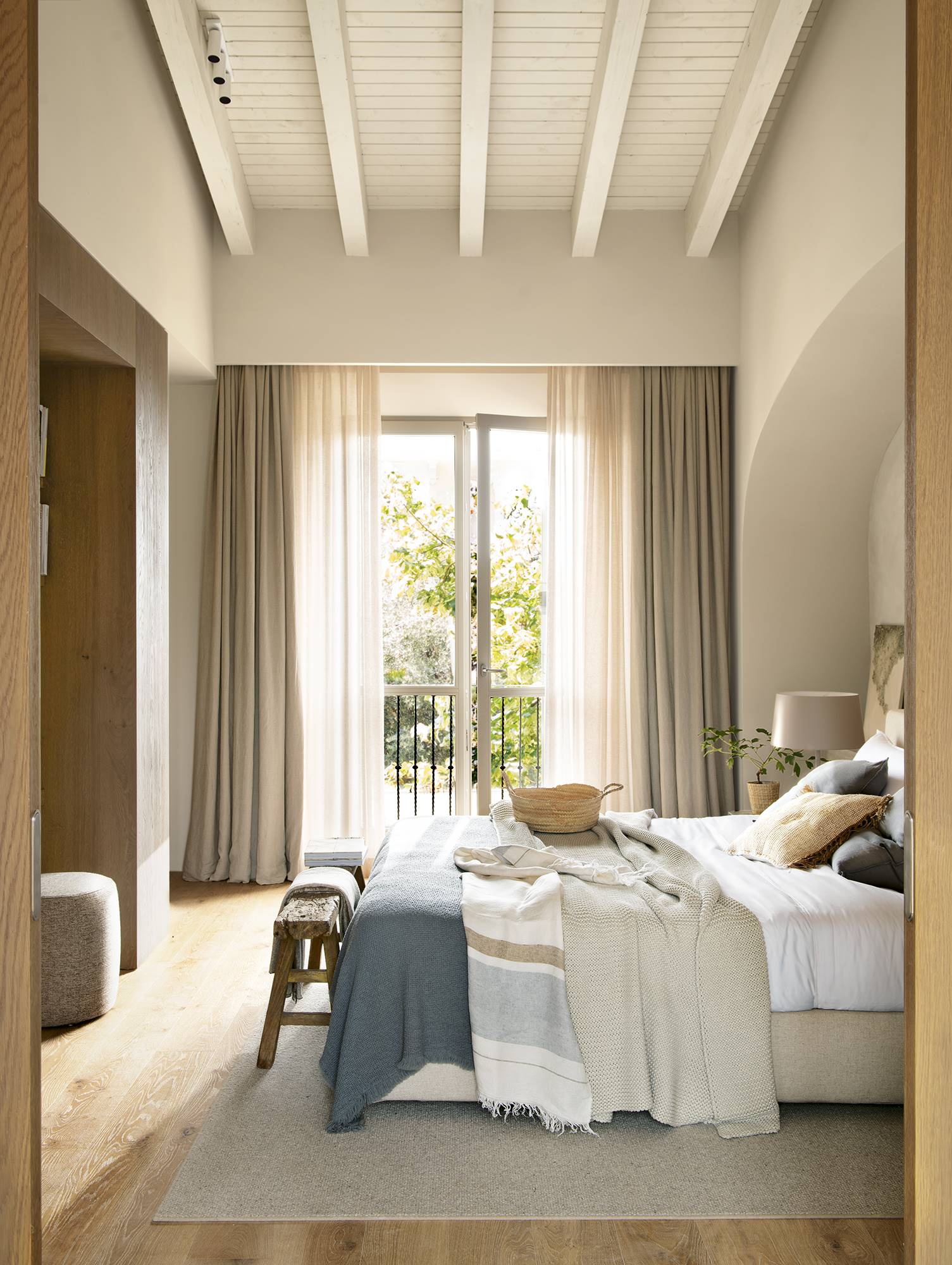 Dormitorio principal con ropa de cama en tonos azules y crudos, y ventanal al fondo con cortinas de lino. 