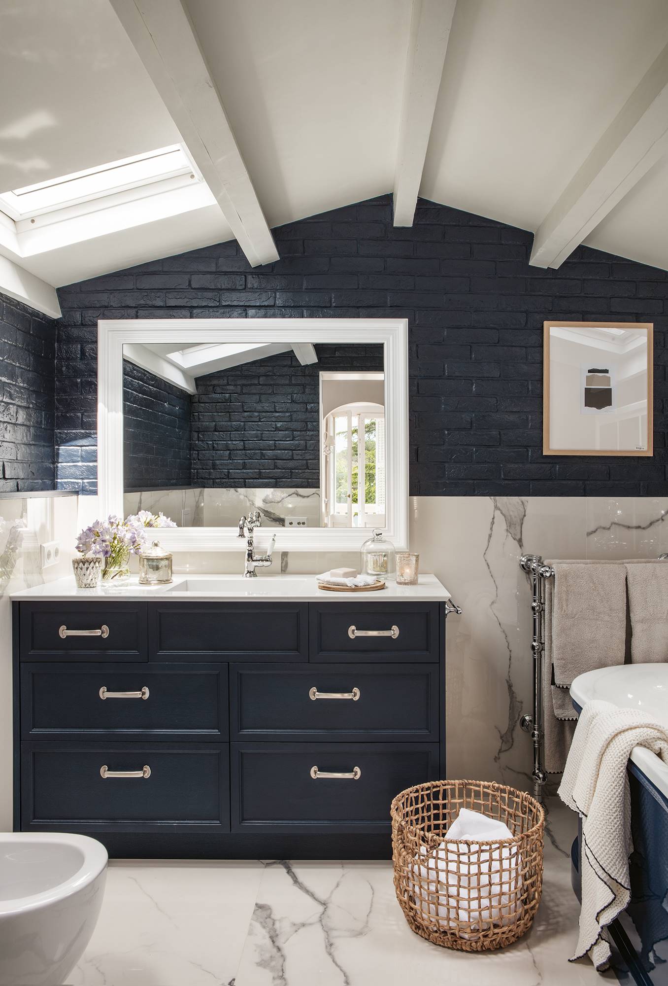 Baño con pared de ladrillo pintado de azul marino, como el mueble, y revestimiento con acabado mármol. 