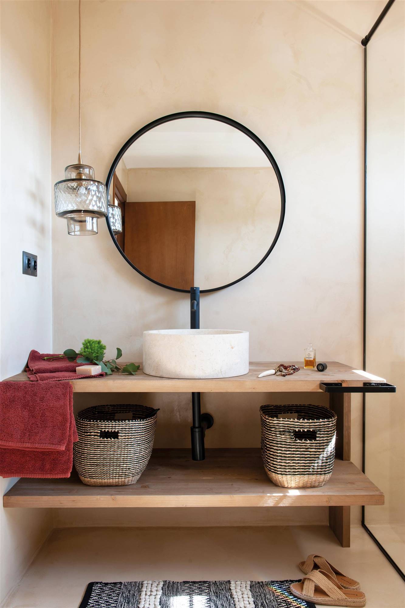 Baño con mueble suspendido en madera clara y espejo redondo negro. 
