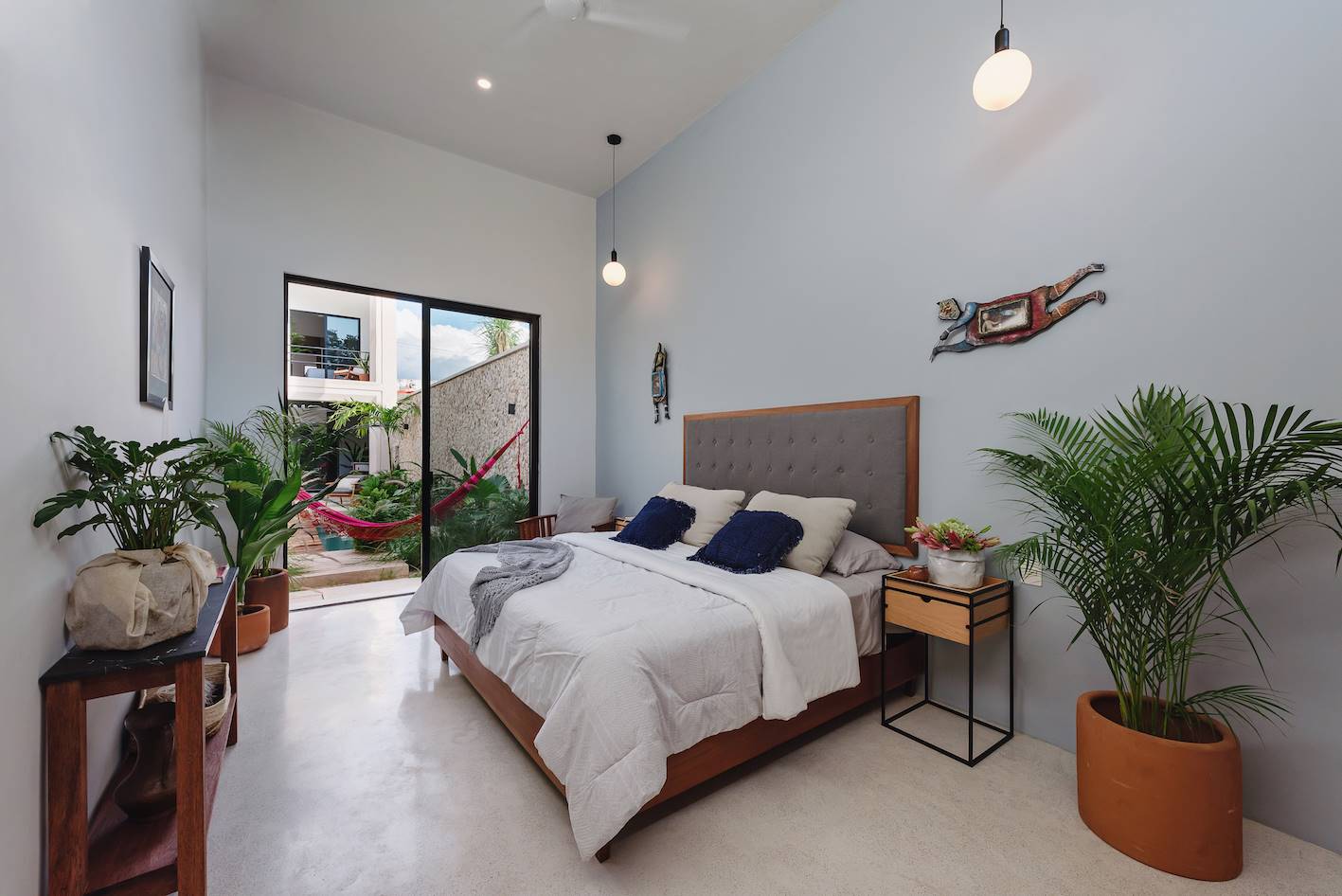 Dormitorio con cabecero de cama de madera y tapizado, plantas de interior y consola.