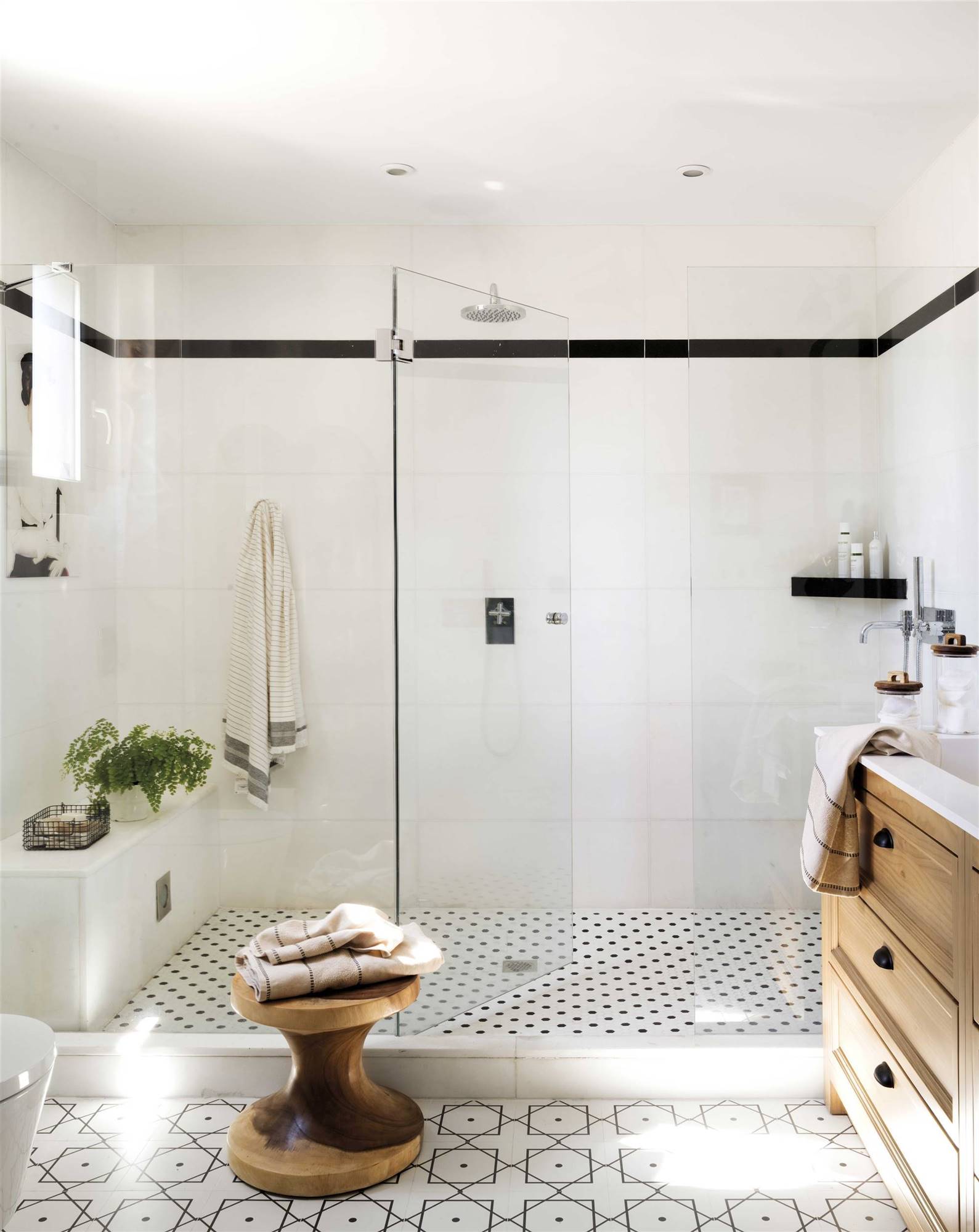 Baño con ducha con las paredes revestidas con azulejos blancos con una cenefa en negro. 