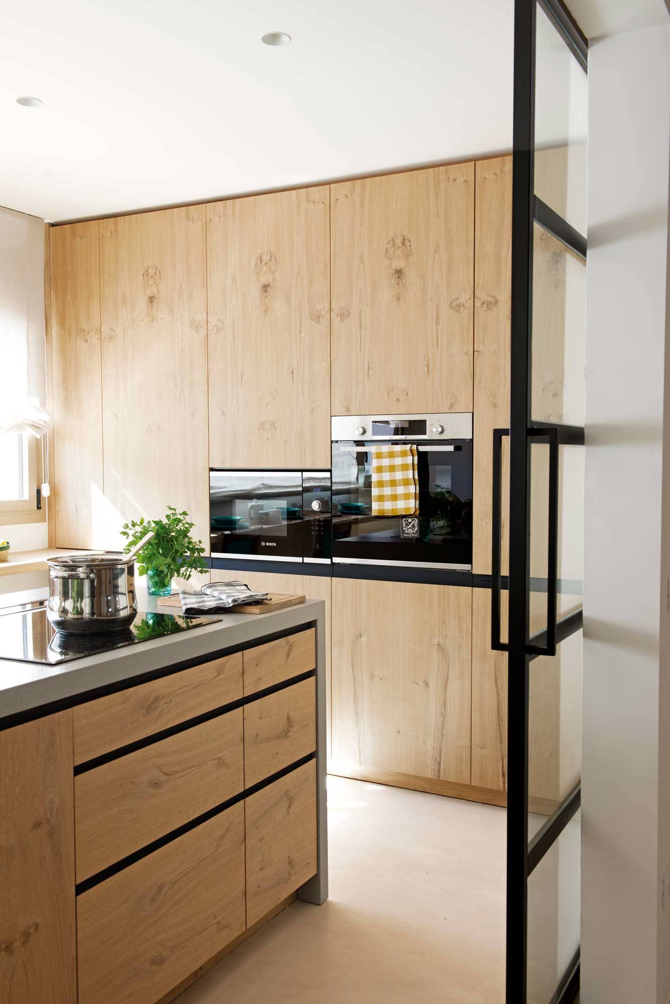 Cocina moderna con muebles panelados con acabado de madera y electrodomésticos eficientes. 