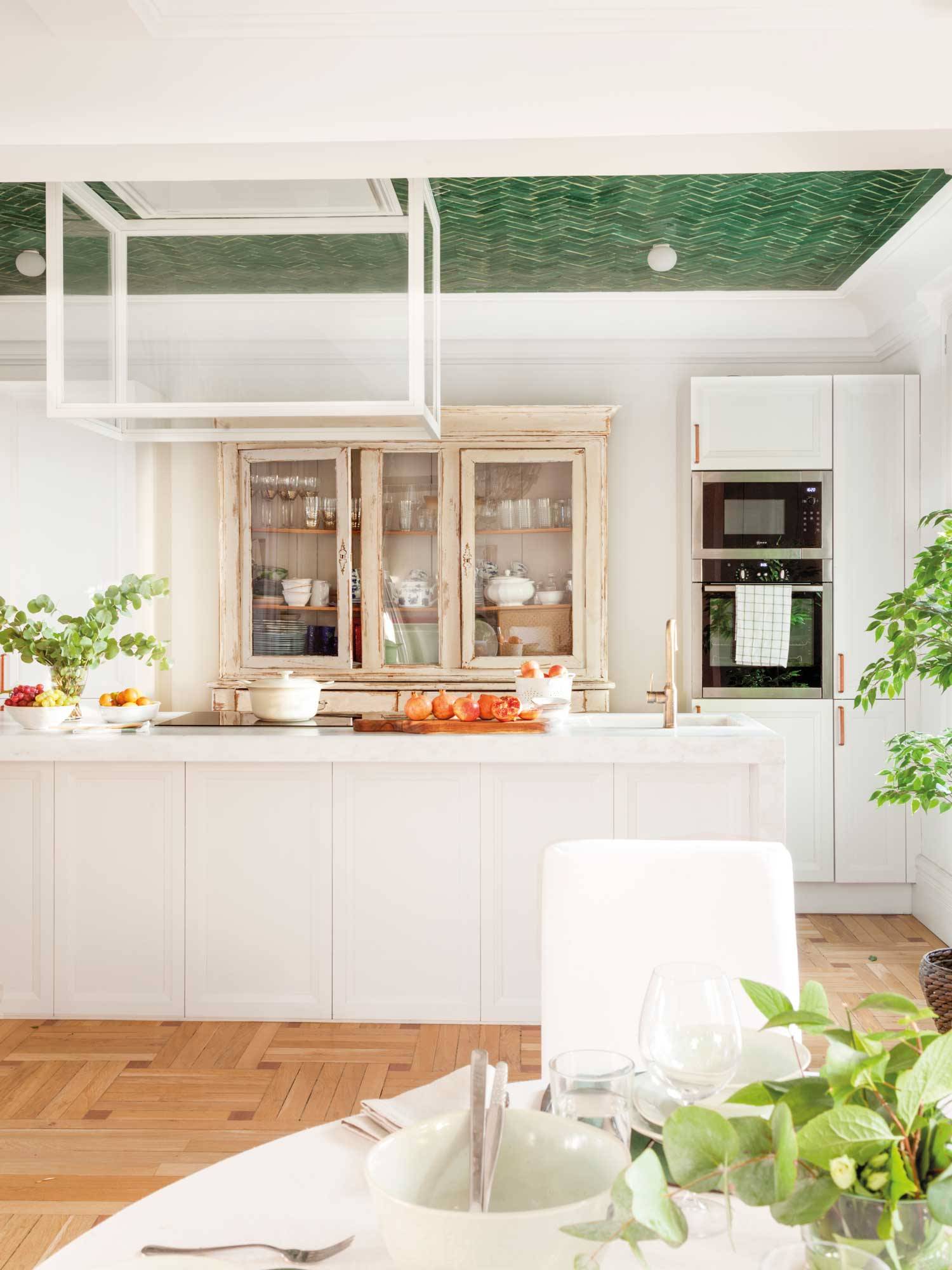 Cocina blanca con isla central, alacena vintage y techo con azulejos verdes. 