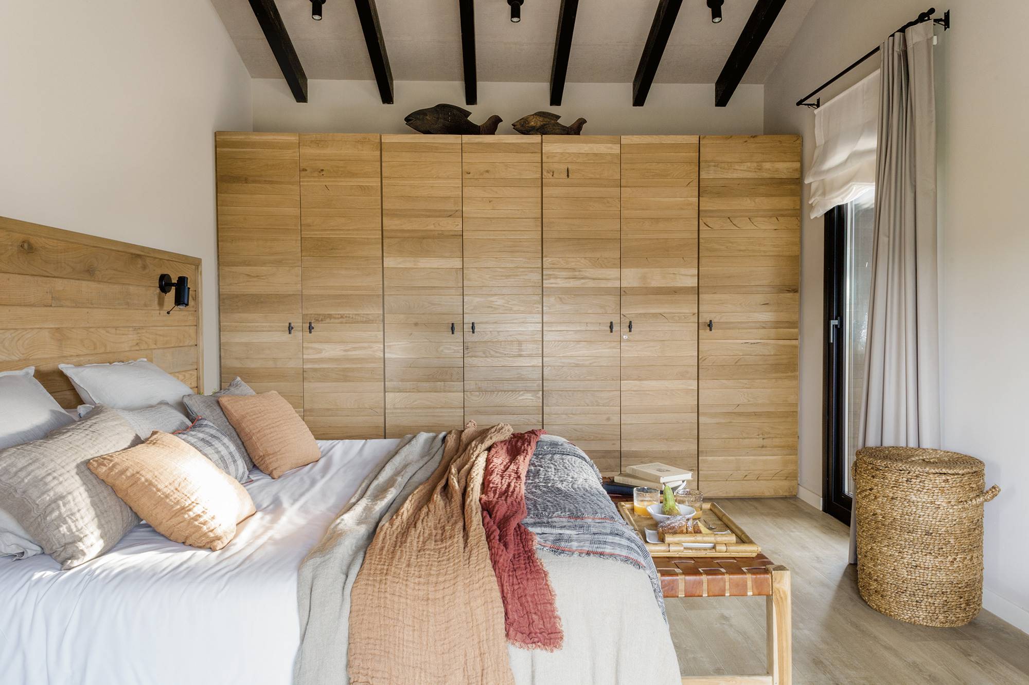 Dormitorio de estilo industrial en una cabaña de montaña, con armario y cabecero de madera, fibras naturales y cuero.