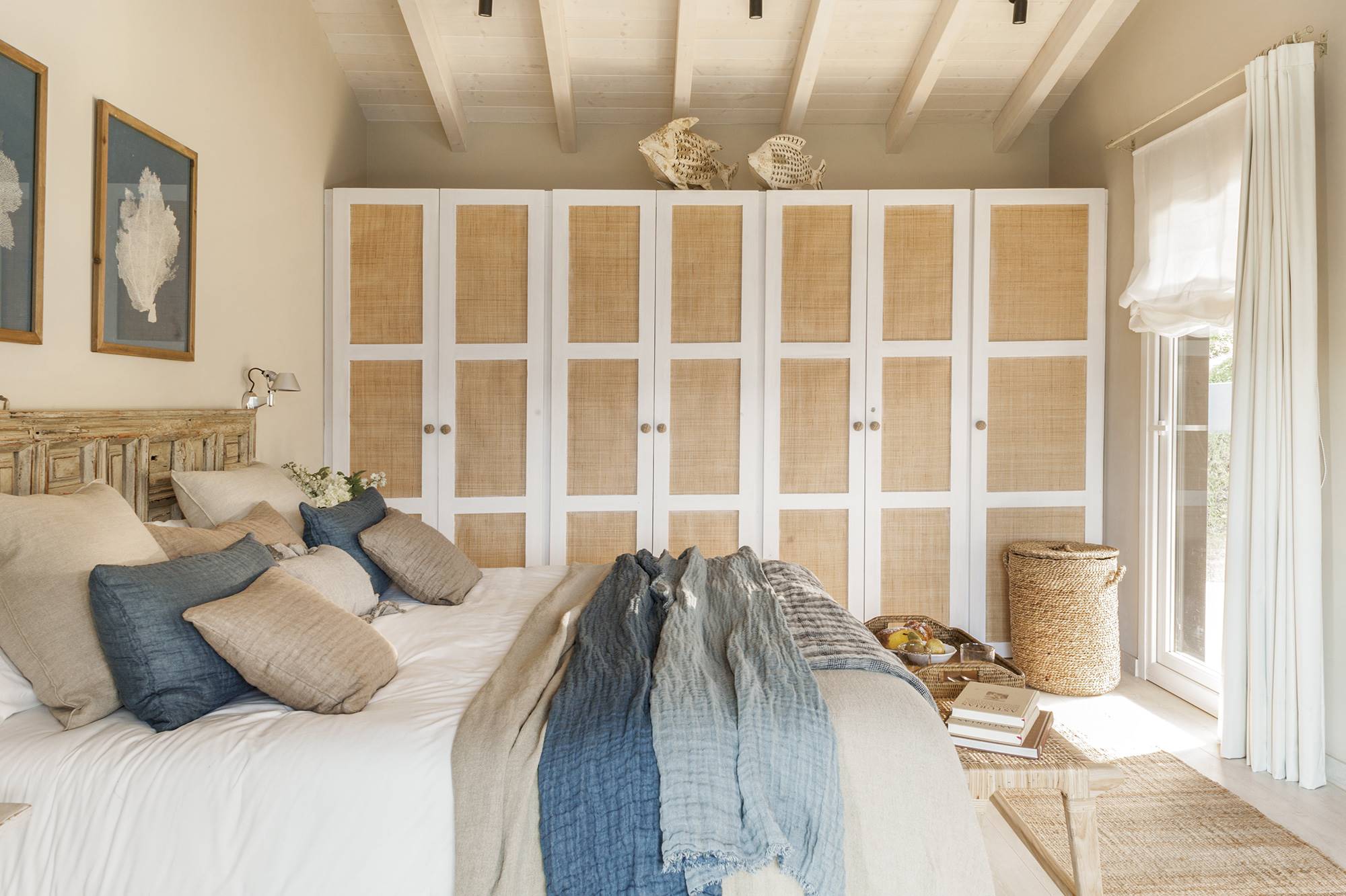 Dormitorio de estilo romántico en una cabaña de montaña, con armario de madera blanca y fibra natural.