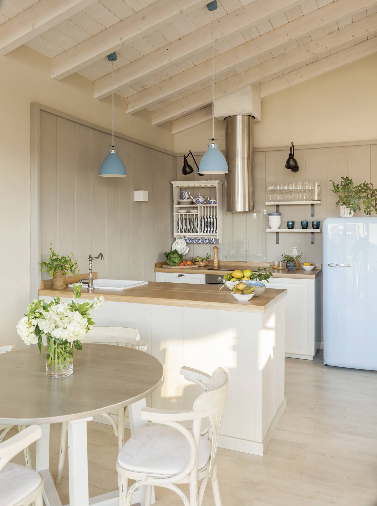 Cocina de estilo romántico con muebles blancos, encimera de roble natural y nevera azul.