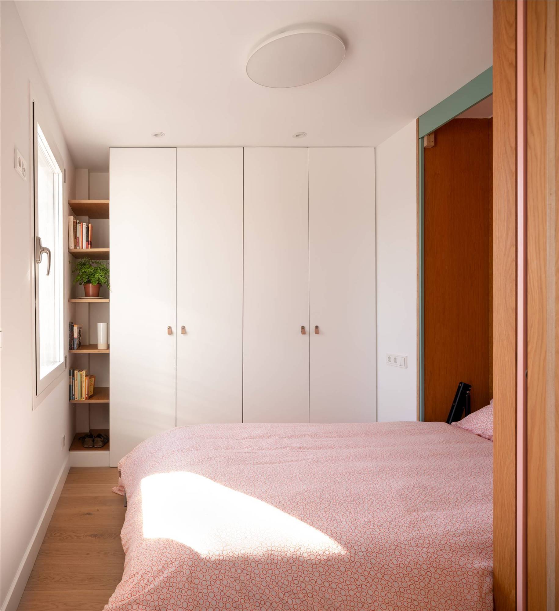 Un pequeño dormitorio con cama abatible con textiles en tonos rosas