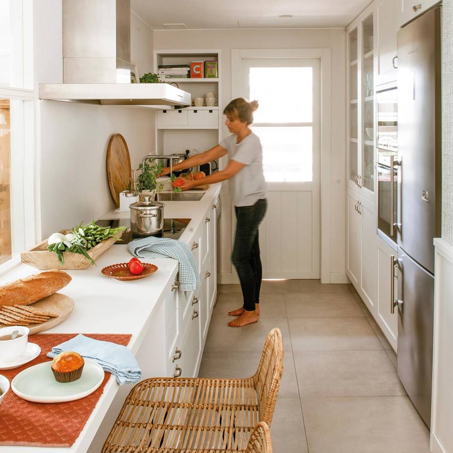 Mujer lavando verduras en una cocina alargada y de color blanco