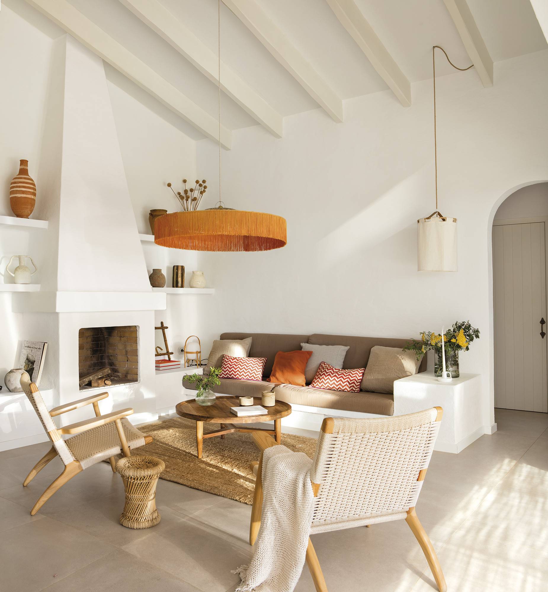 Salón blanco con chimenea, sofá de obra, lámpara naranja y butacas de cuerda