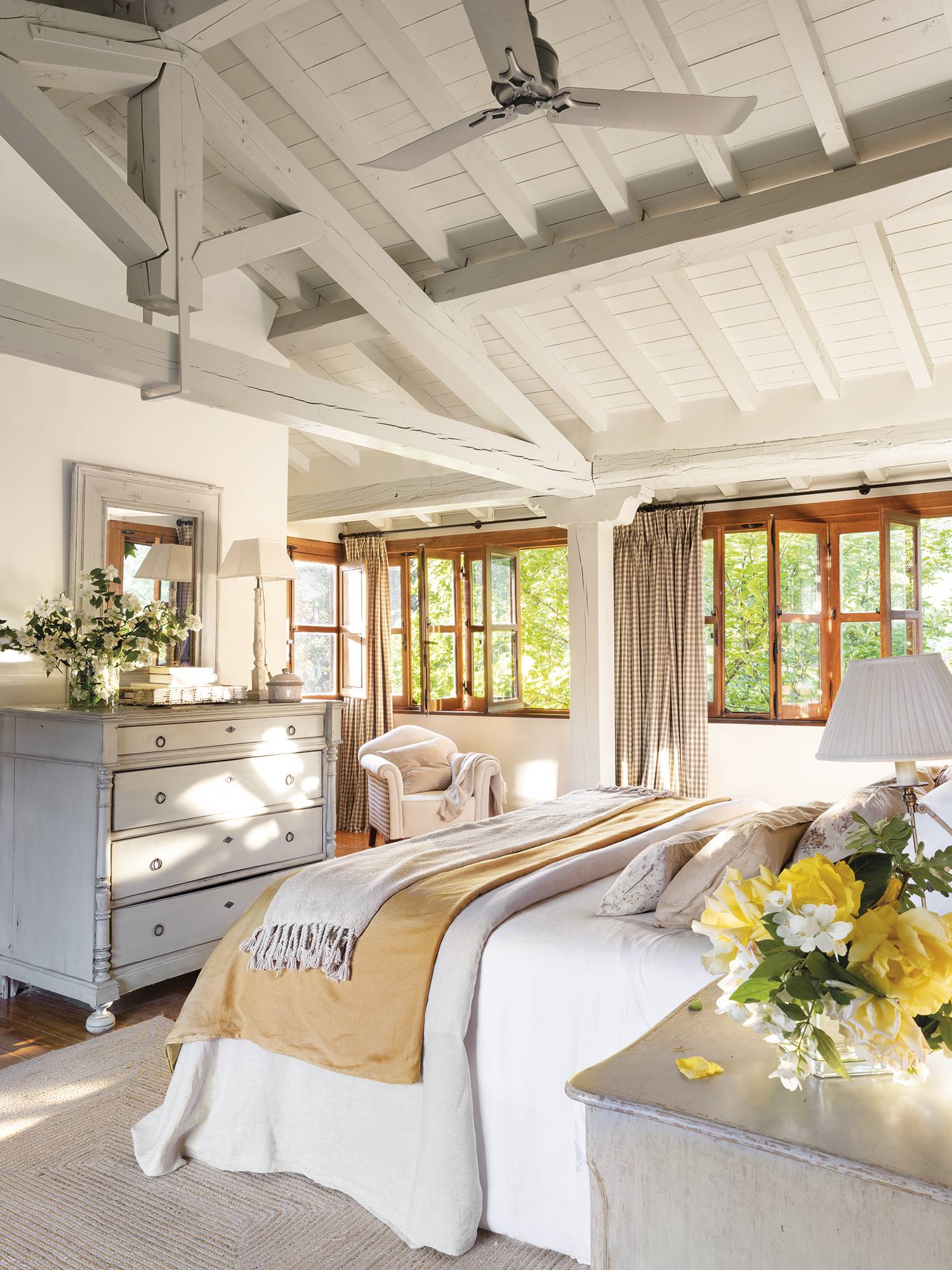 Dormitorio rodeado de ventanas con vigas de madera y cómoda.