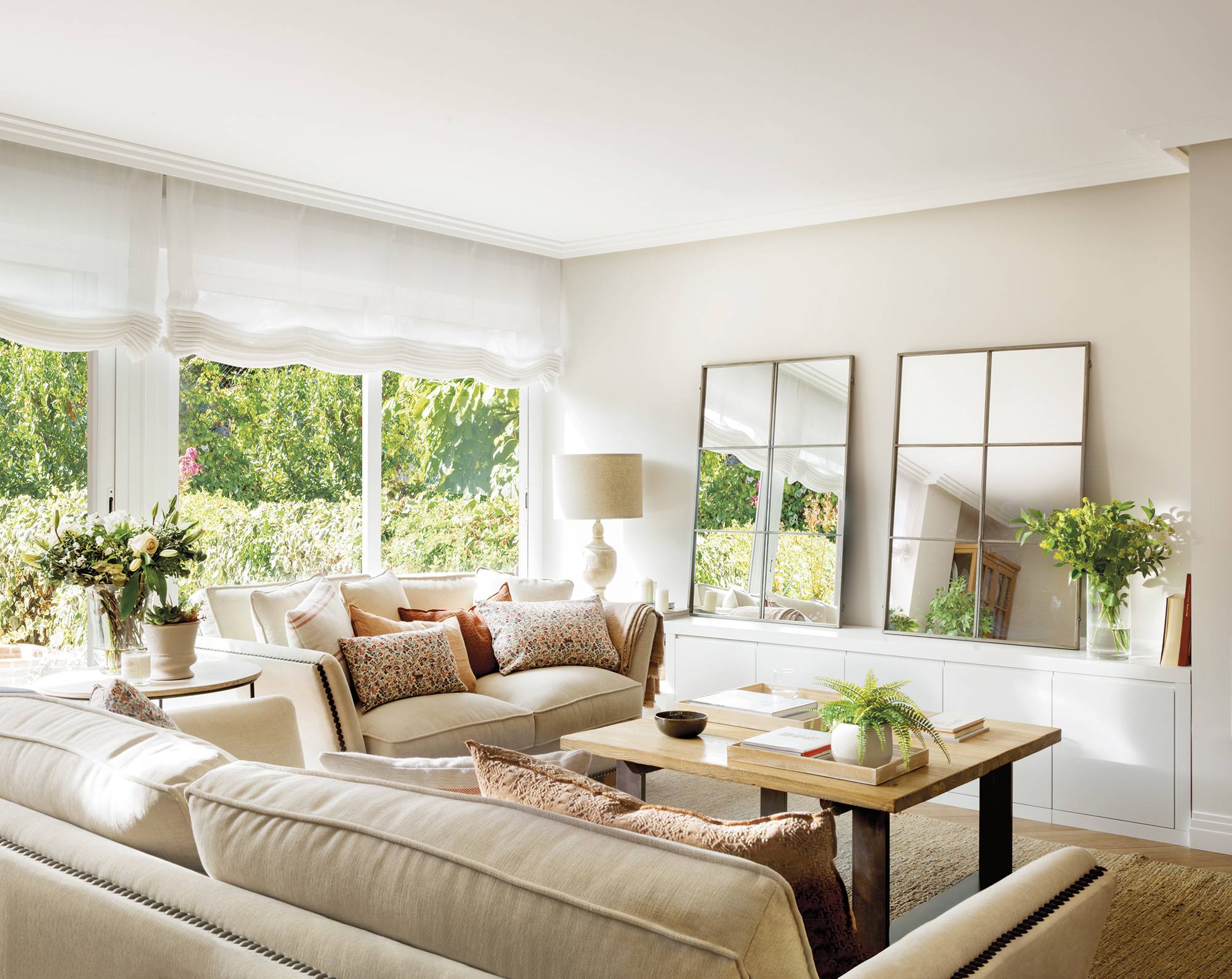 Salón con sofás de color beige, mueble blanco y espejos tipo ventana. 