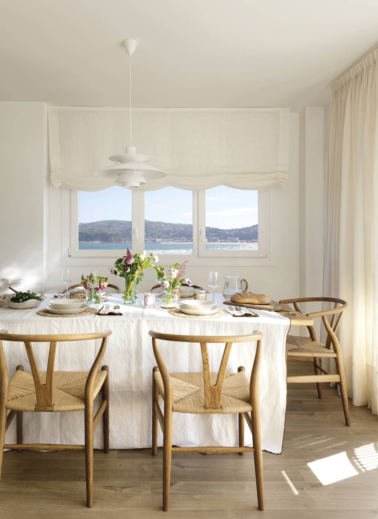 Comedor blanco con ventana, mesa de madera y sillas de fibras. 