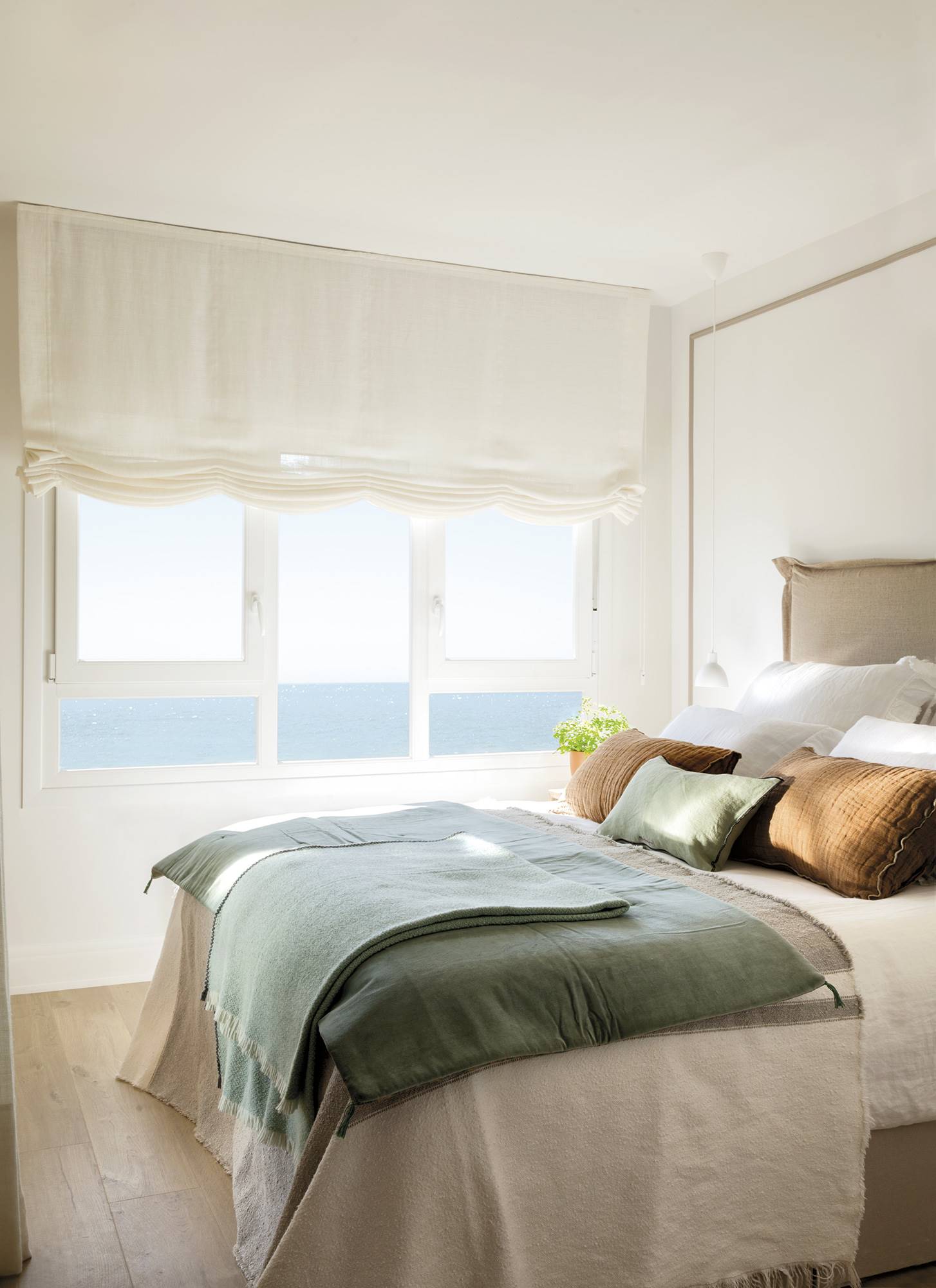 Dormitorio con cama, cabecero tapizado y ventana con estores de lino.