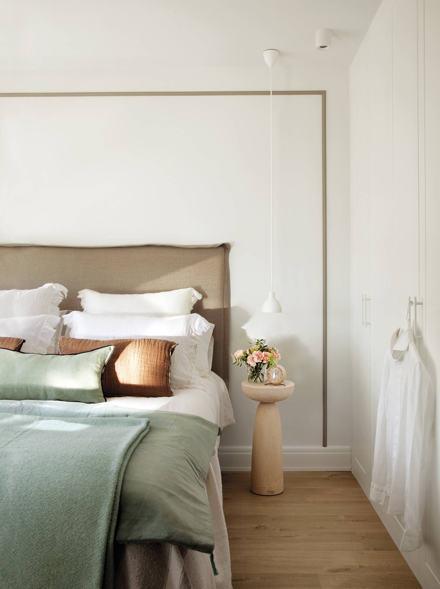 Dormitorio principal con cabecero tapizado, mesa auxiliar de madera y ropa de cama de lino.