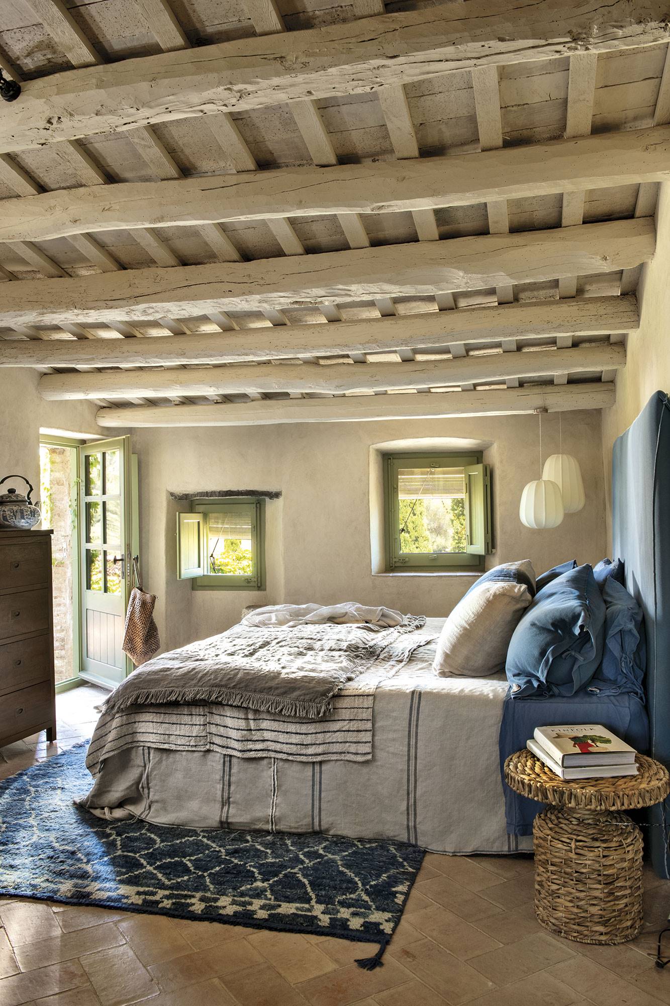 Dormitorio con cabecero tapizado azul, alfombra azul, mesita de fibras y vigas de madera