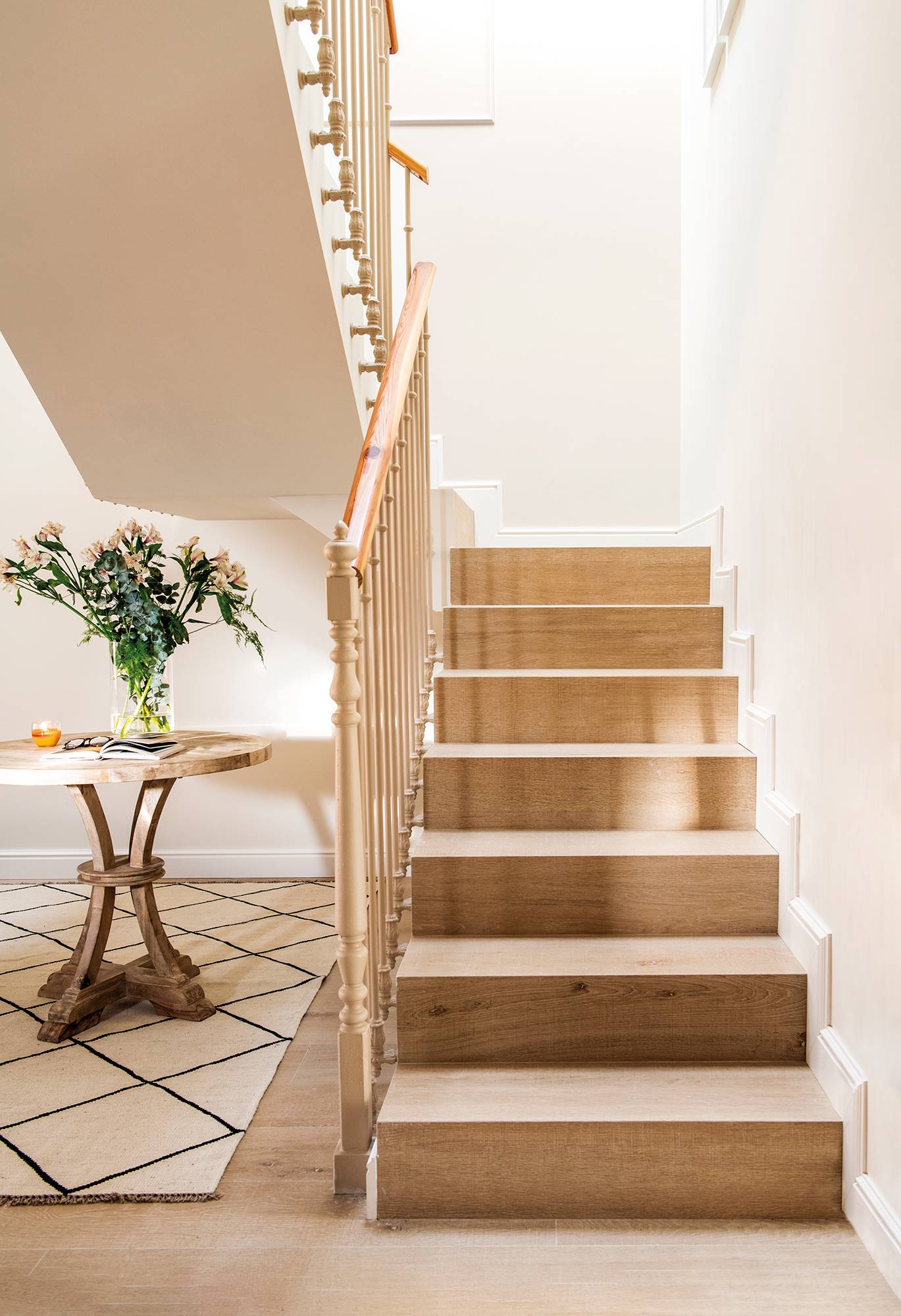 Detalle de zona de paso con escalera revestida en madera y paredes en color blanco. 