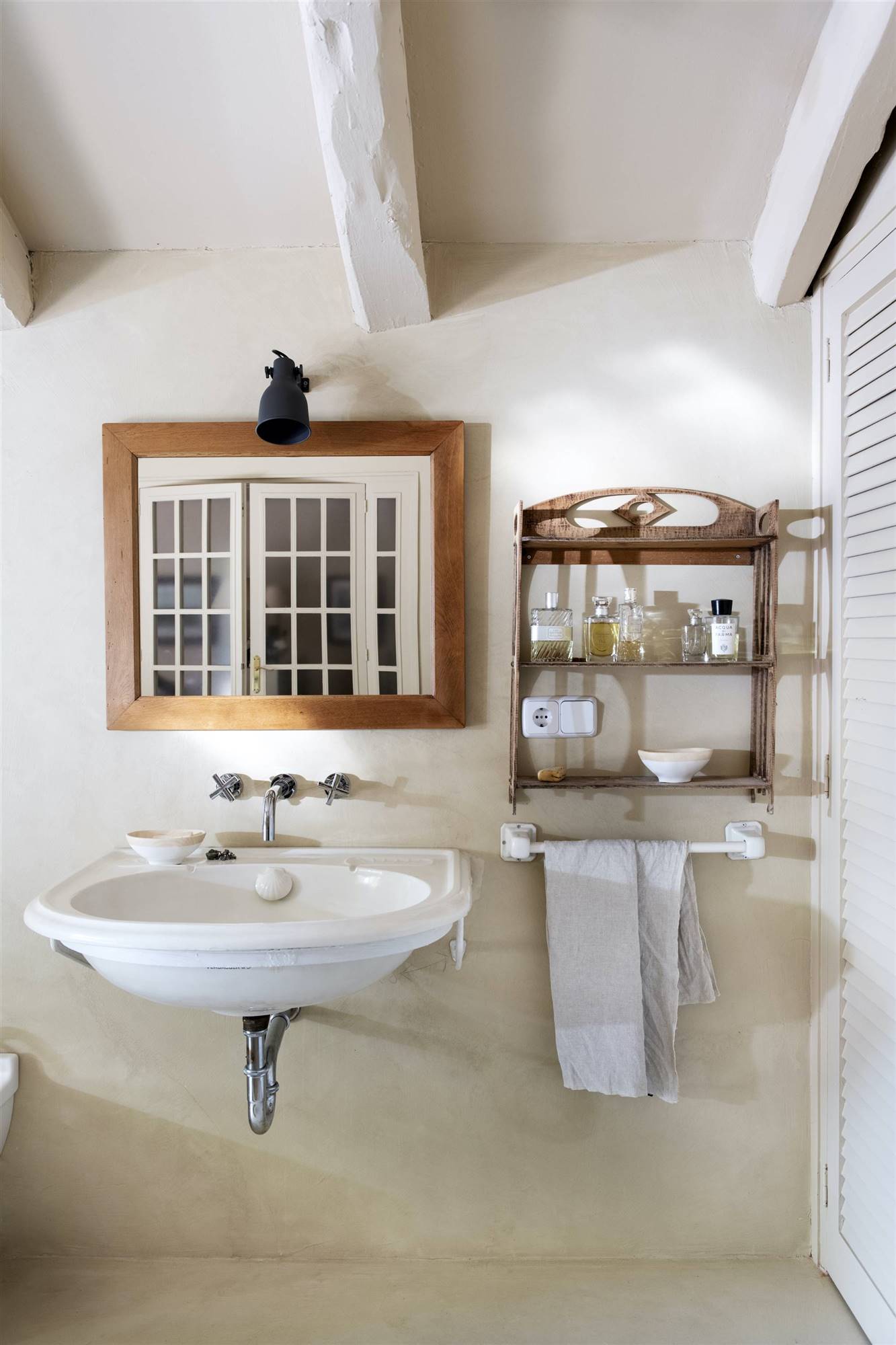 Baño con lavabo suspendido y espejo de madera, revestimiento y pavimento de microcemento. 
