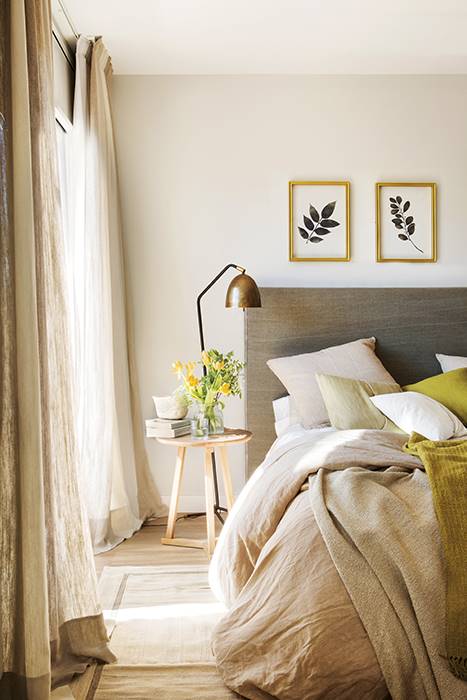 Dormitorio con cabecero tapizado y textiles en tonos neutros. 
