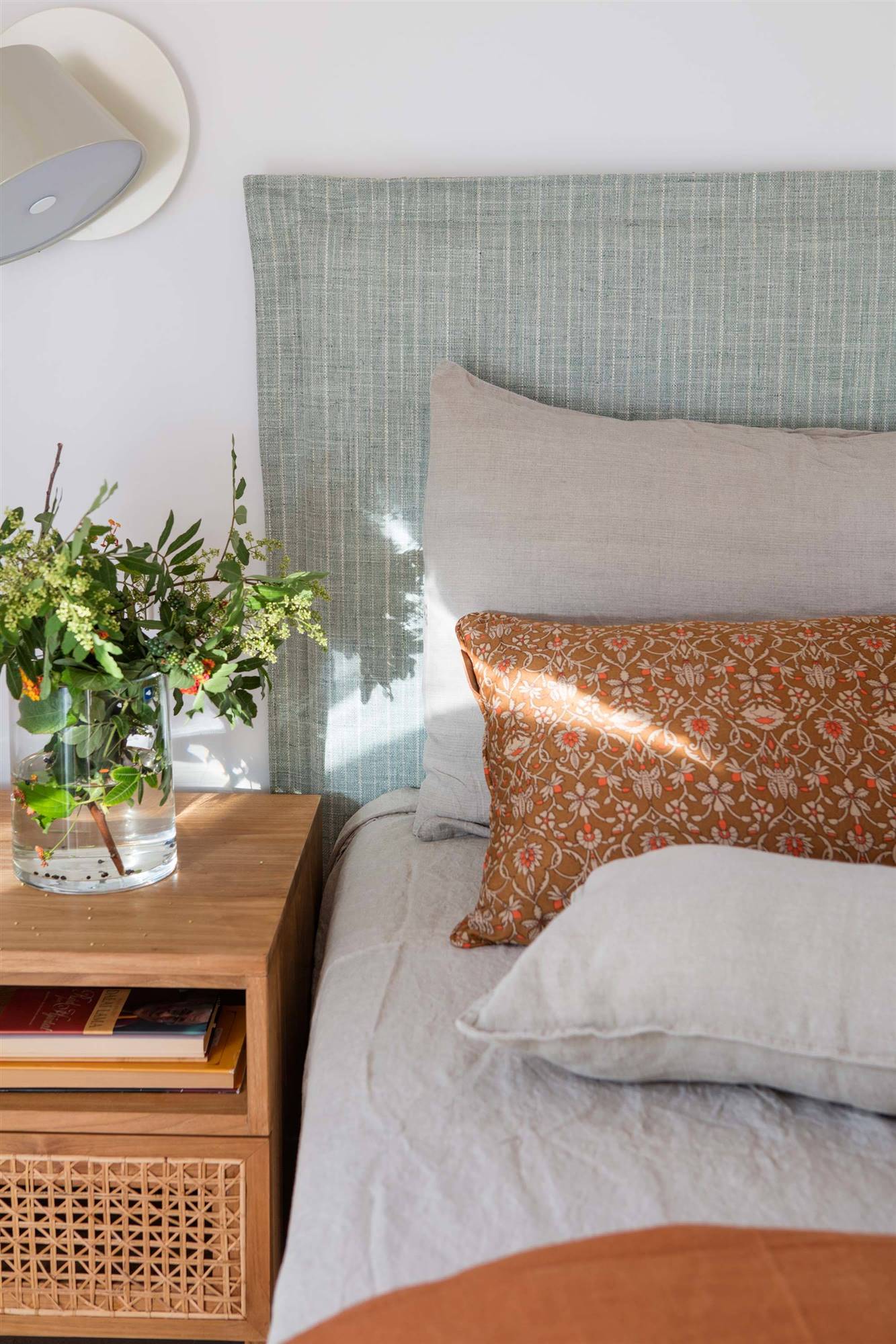 Dormitorio con cabecero con funda de lino gris y ropa de cama blanca y naranja. 
