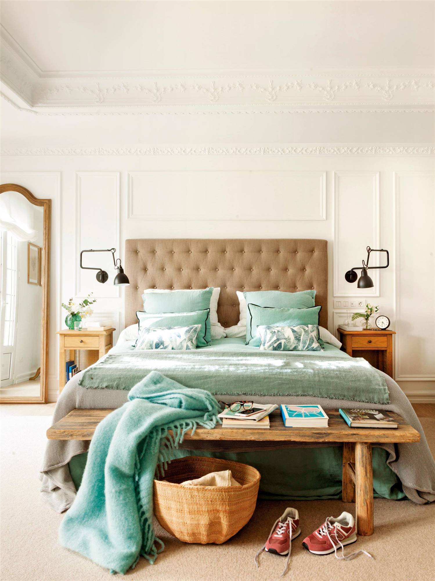 Dormitorio con cabecero de capitoné, banco de madera y molduras en pared.