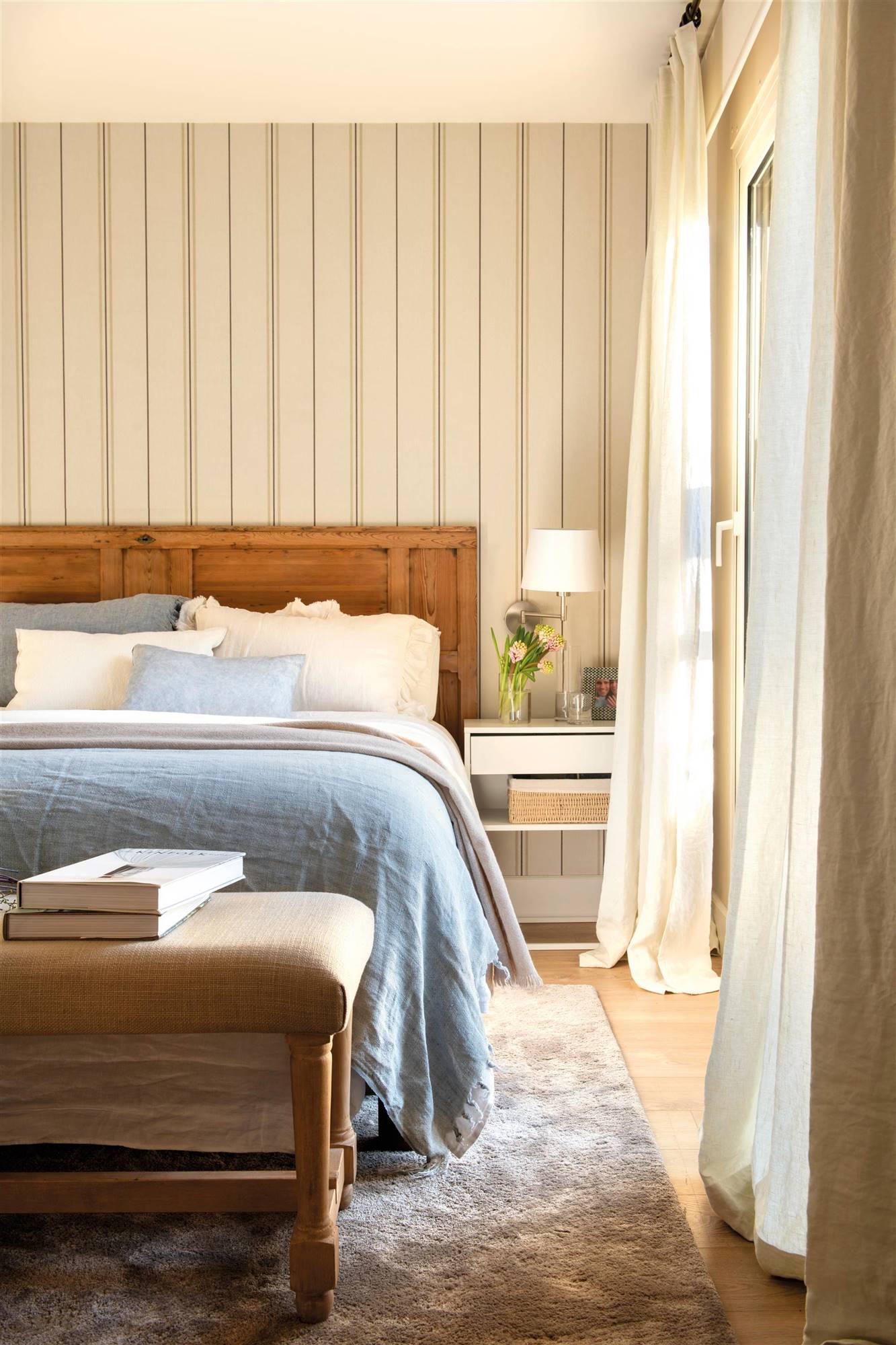 Dormitorio con puerta de madera recuperada como cabecero y papel pintado a rayas.