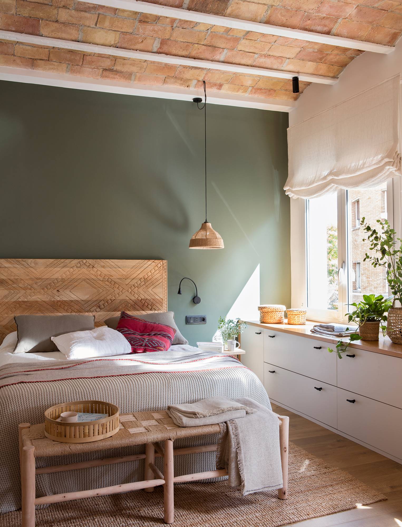 Dormitorio moderno con pared del cabecero en verde y estor en ventana. 