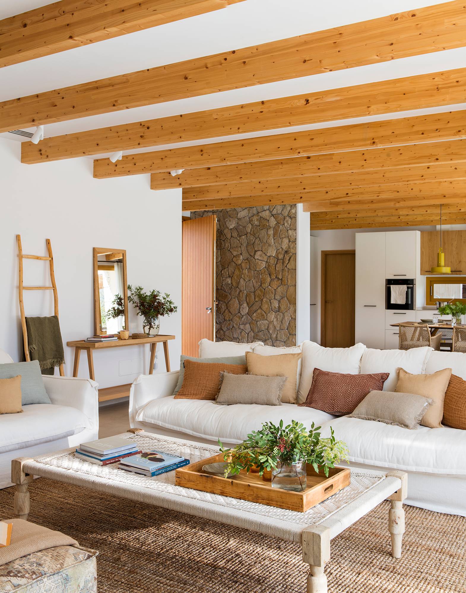 Salón con sofá blanco, vigas de madera en techo y pared de piedra vista