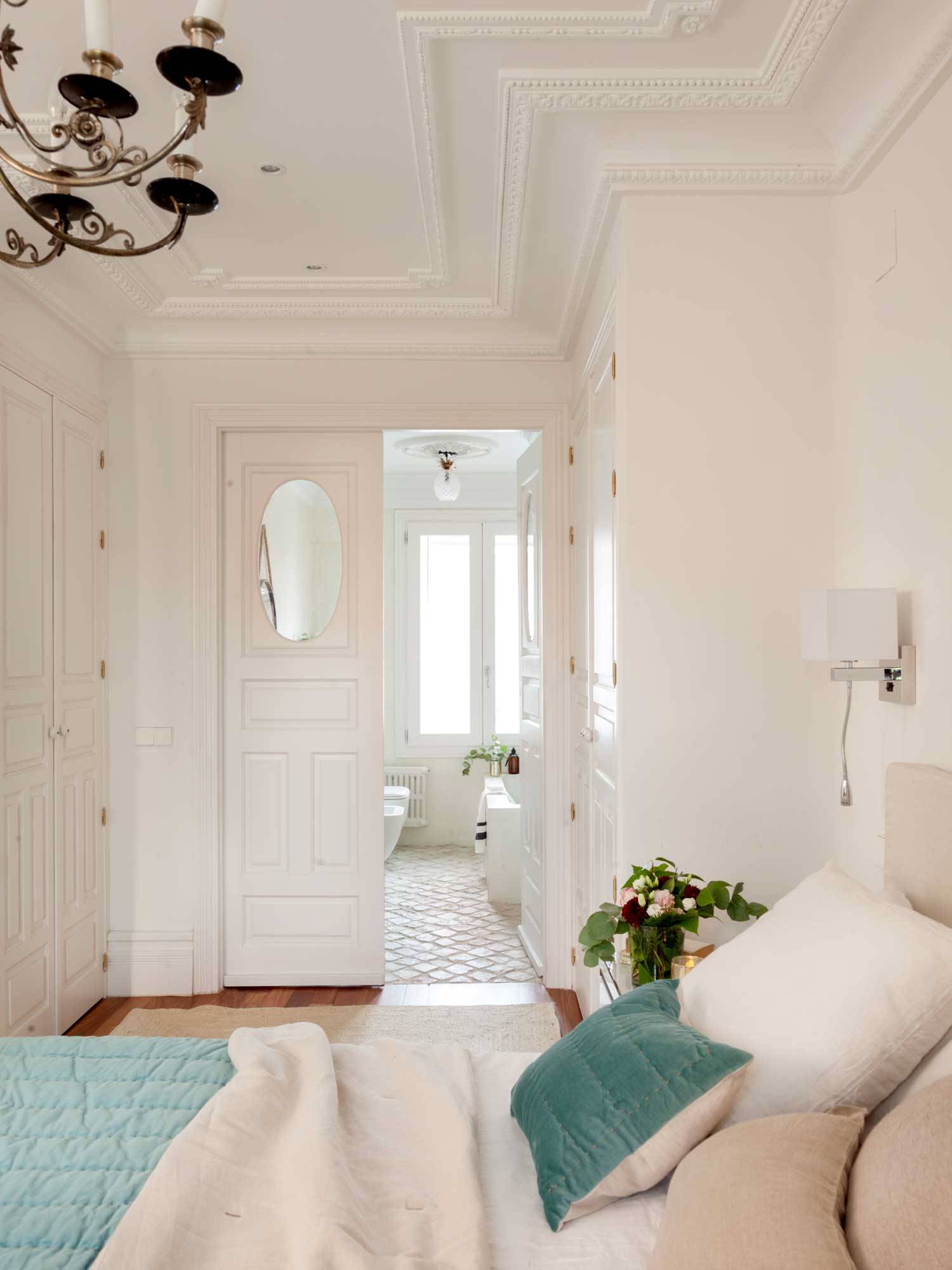 Dormitorio con puerta blanca con molduras y cristal ovalado a modo de ventana que conecta con el baño en suite.