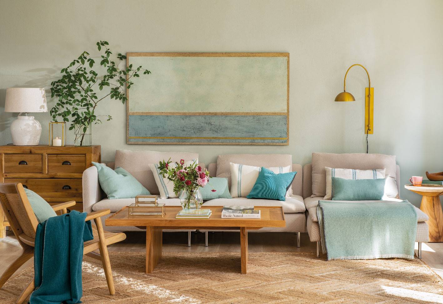 Salón con mesa de centro y butaca de madera, sofá gris y textiles en tonos verdes y azules.