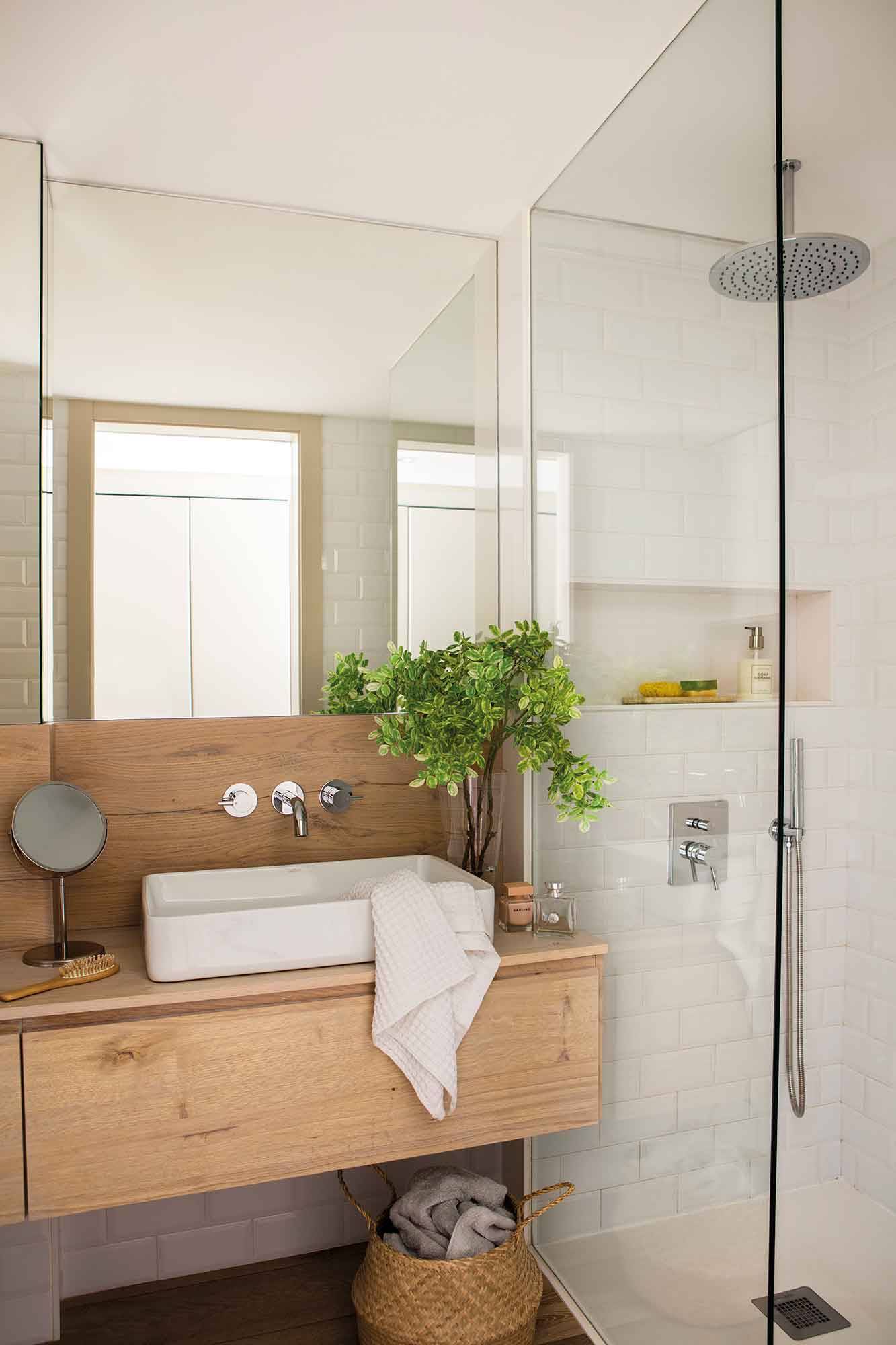Baño con mueble de madera y gran espejo sin marco. 