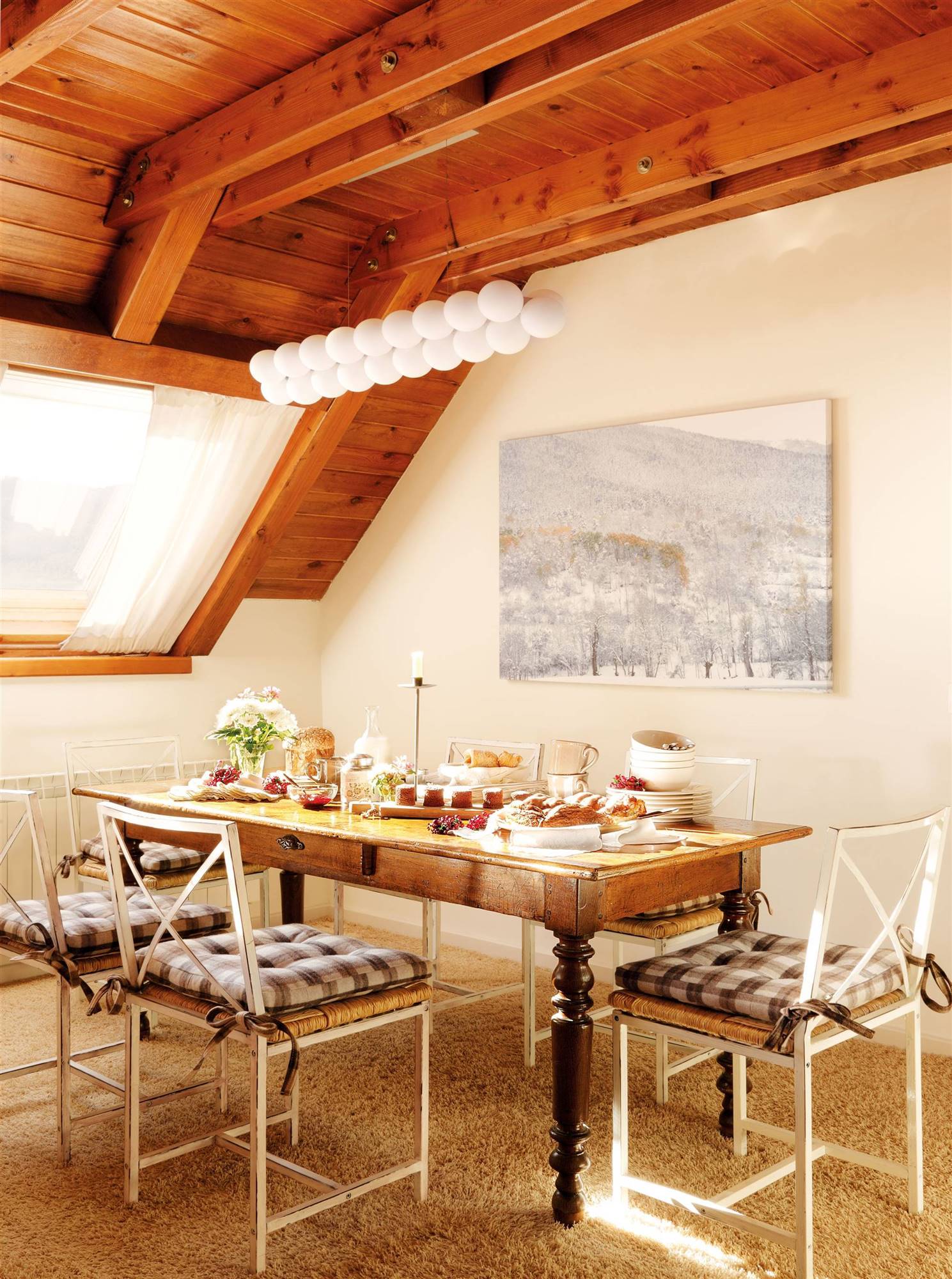 Comedor rústico con mesa de madera, vigas y pintura de paisaje. 