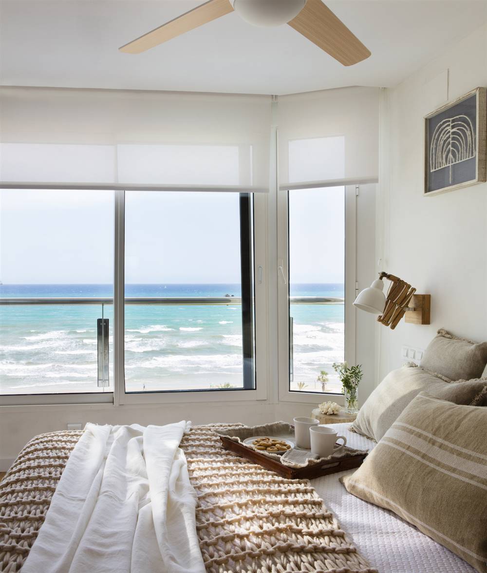 Dormitorio con vistas al mar a través de ventanales con estores. 