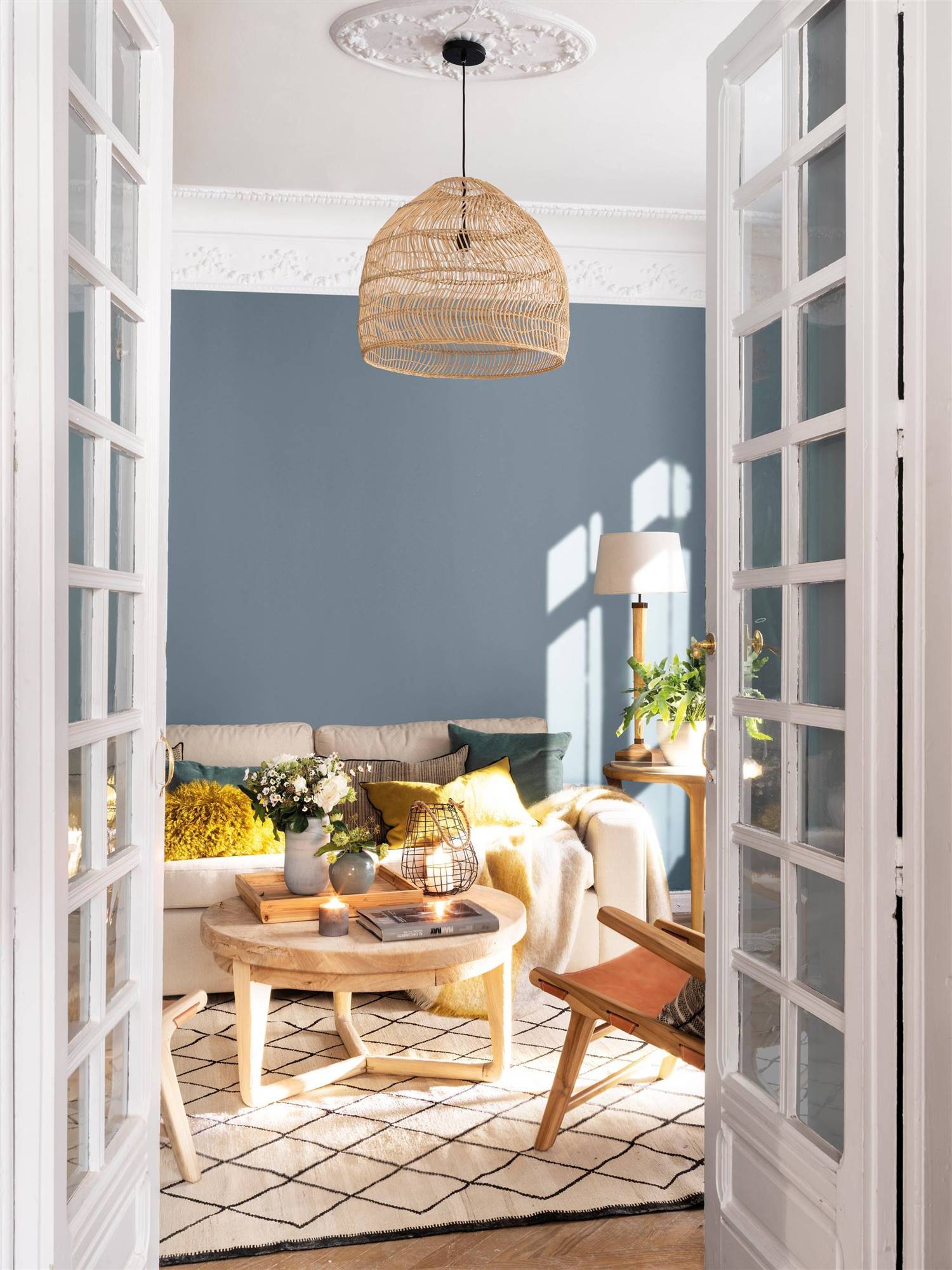 Salón pintado de azul grisáceo y decorado con sofá blanco, mesa de madera y alfombra geométrica. 