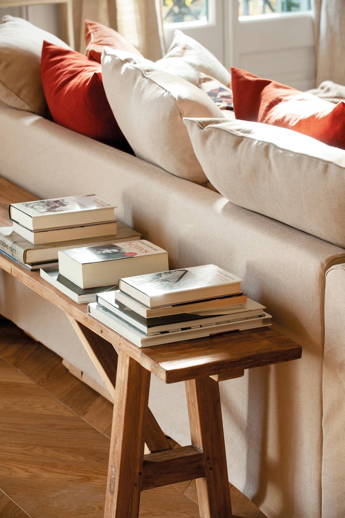 Banco de madera con libros detrás del sofá.