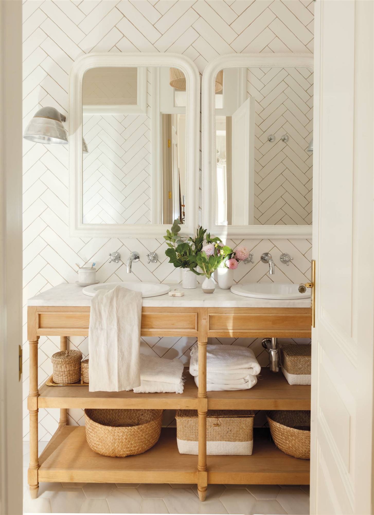 Baño con azulejos tipo metro en diagonal, mueble de madera y espejos con marcos blancos. 