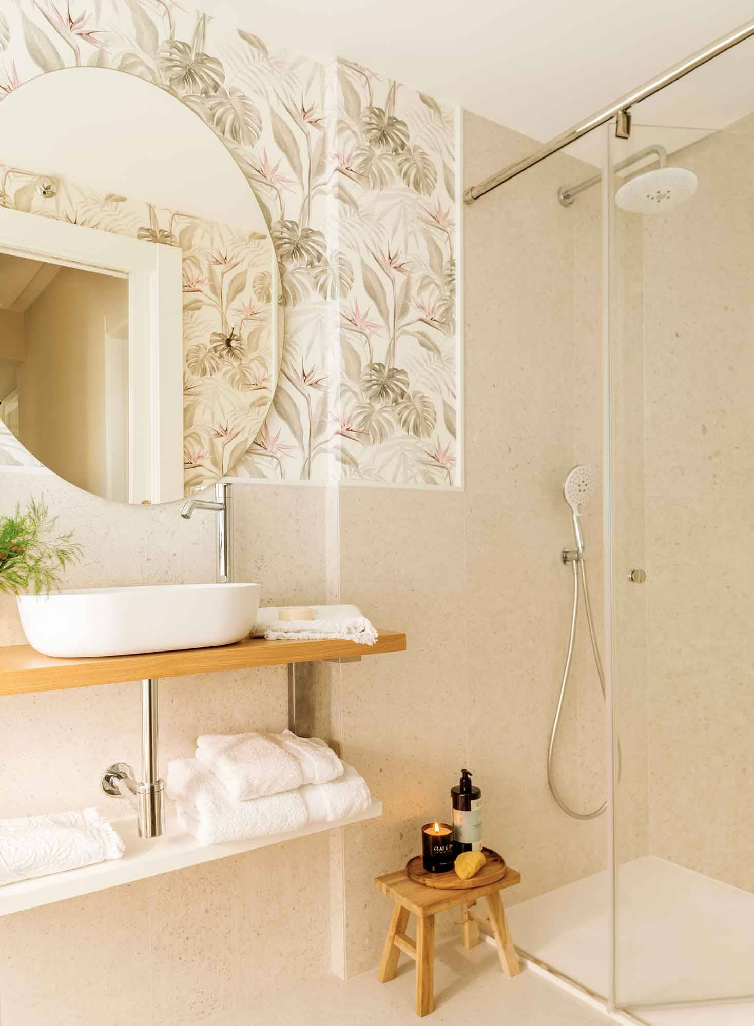 Baño pequeño con papel pintado y espejo ovalado sin marco. 
