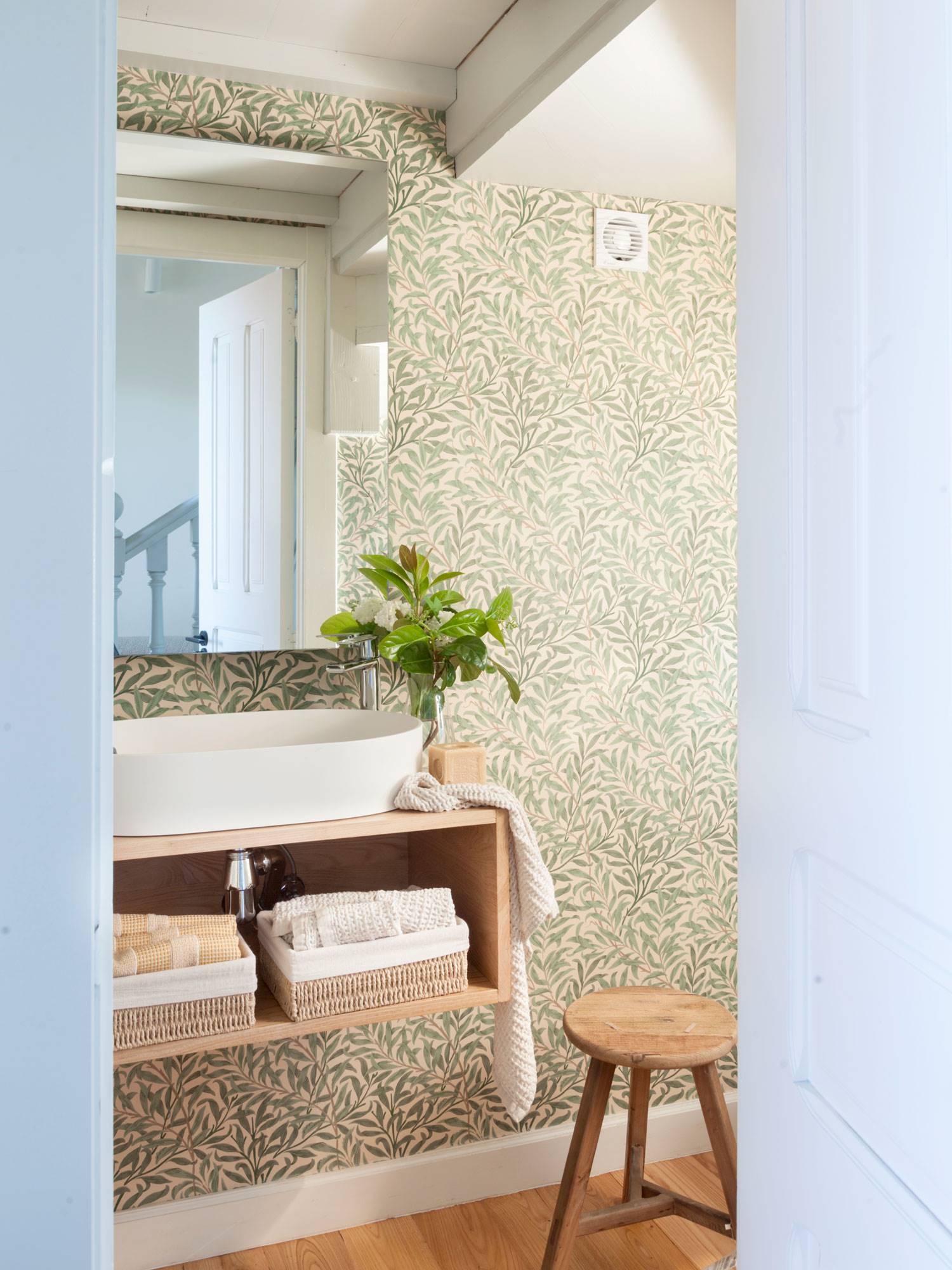 Baño con papel pintado floral y espejo con marco biselado. 