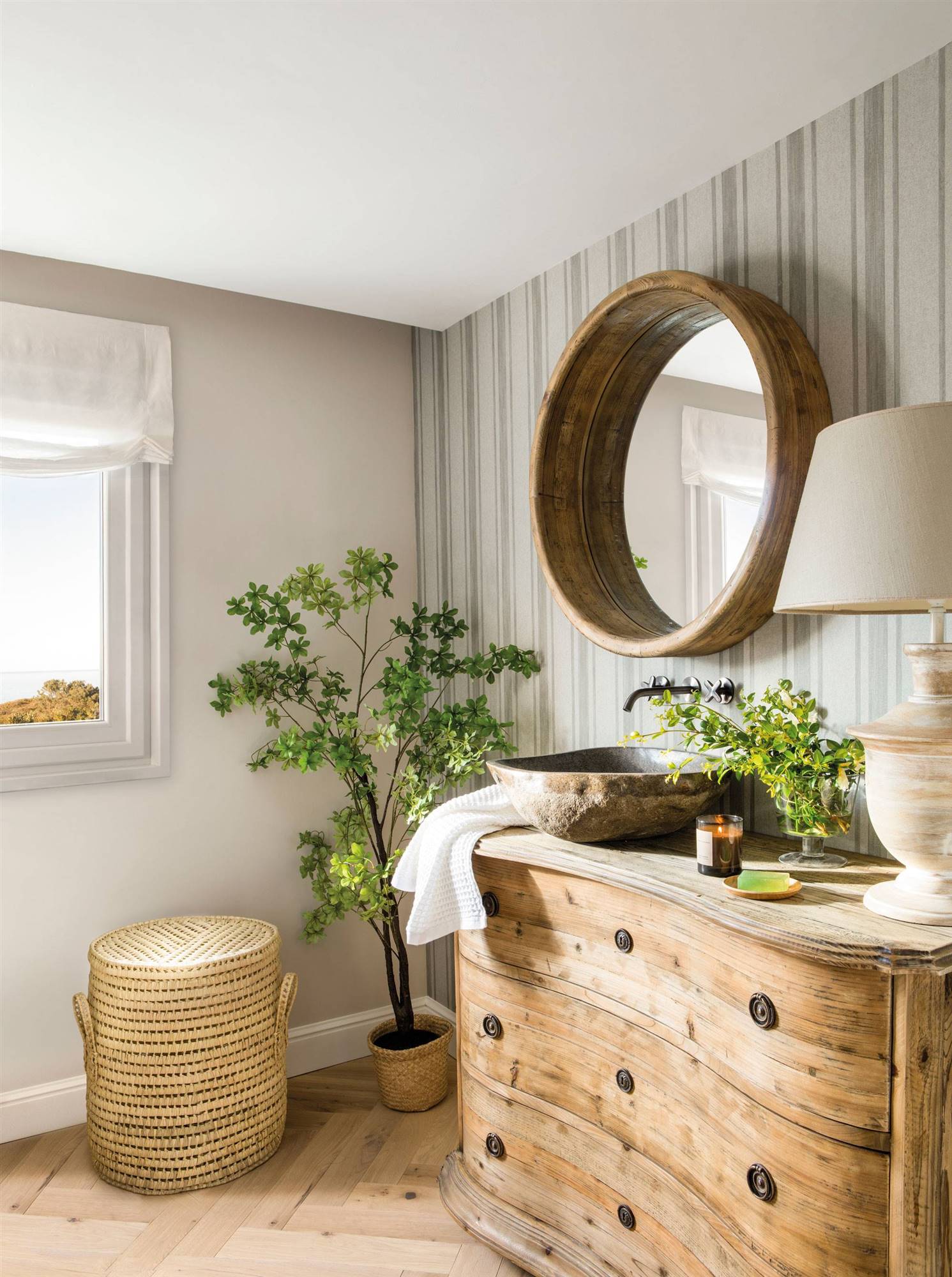 Baño de estilo rústico con cómoda antigua a modo de mueble bajolavabo y espejo redondo con marco de madera. 