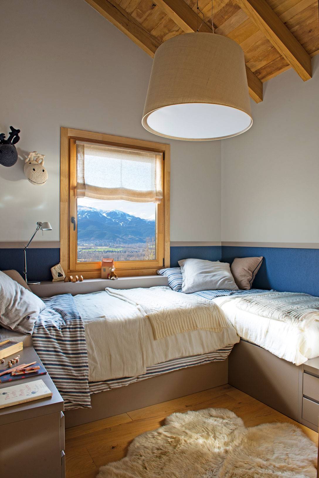 Dormitorio infantil pequeño con dos camas, arrimadero azul y techo abuhardillado.