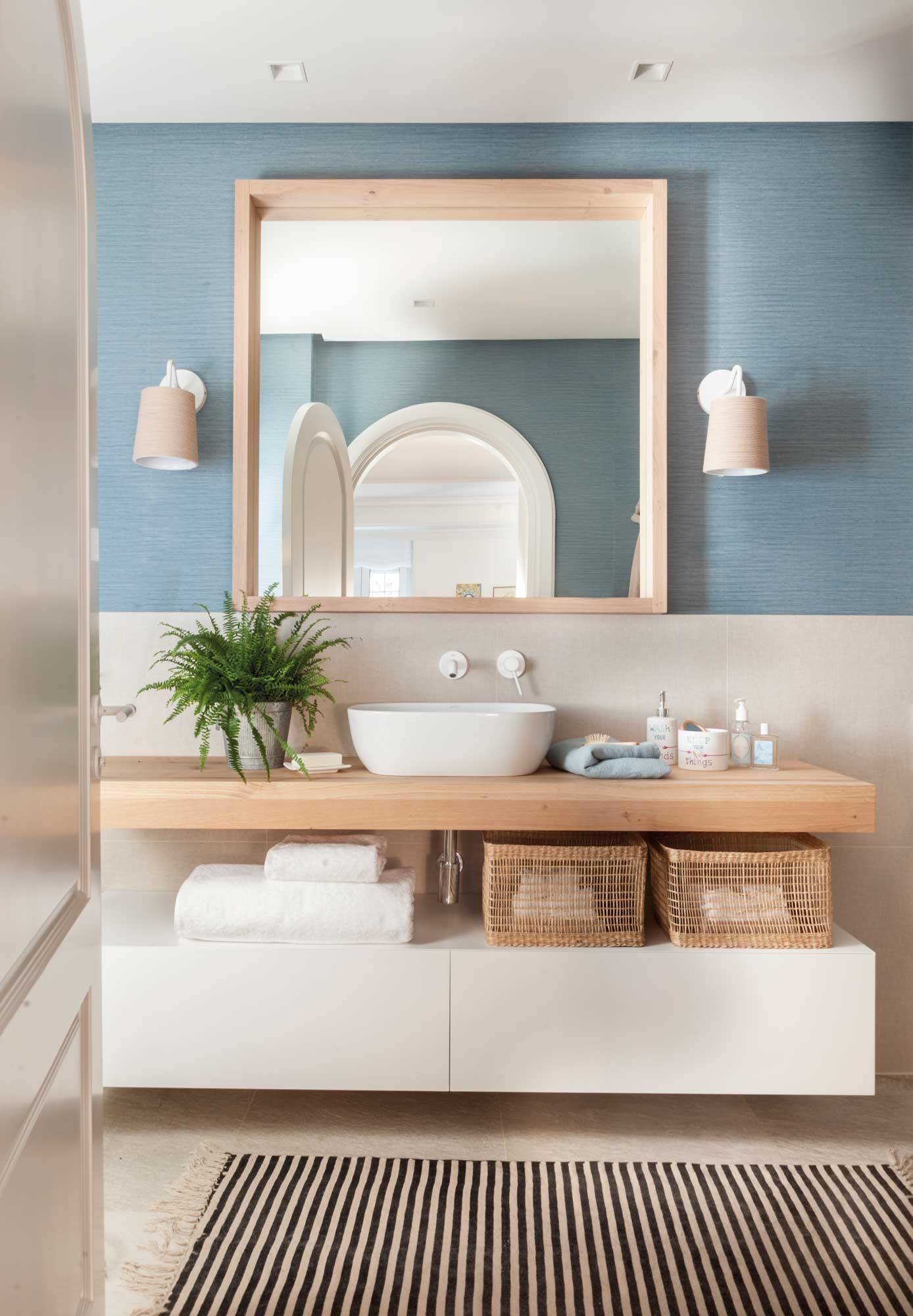 Baño con mueble blanco y encimera en madera y papel pintado textil en azul. 