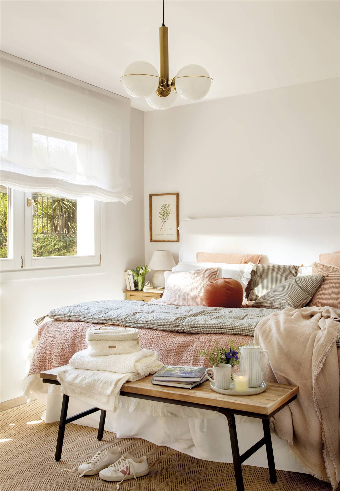 Dormitorio con cama de color blanco, estores blancos, lámpara de techo con bolas, ropa de cama en tonos rosados y banco a los pies