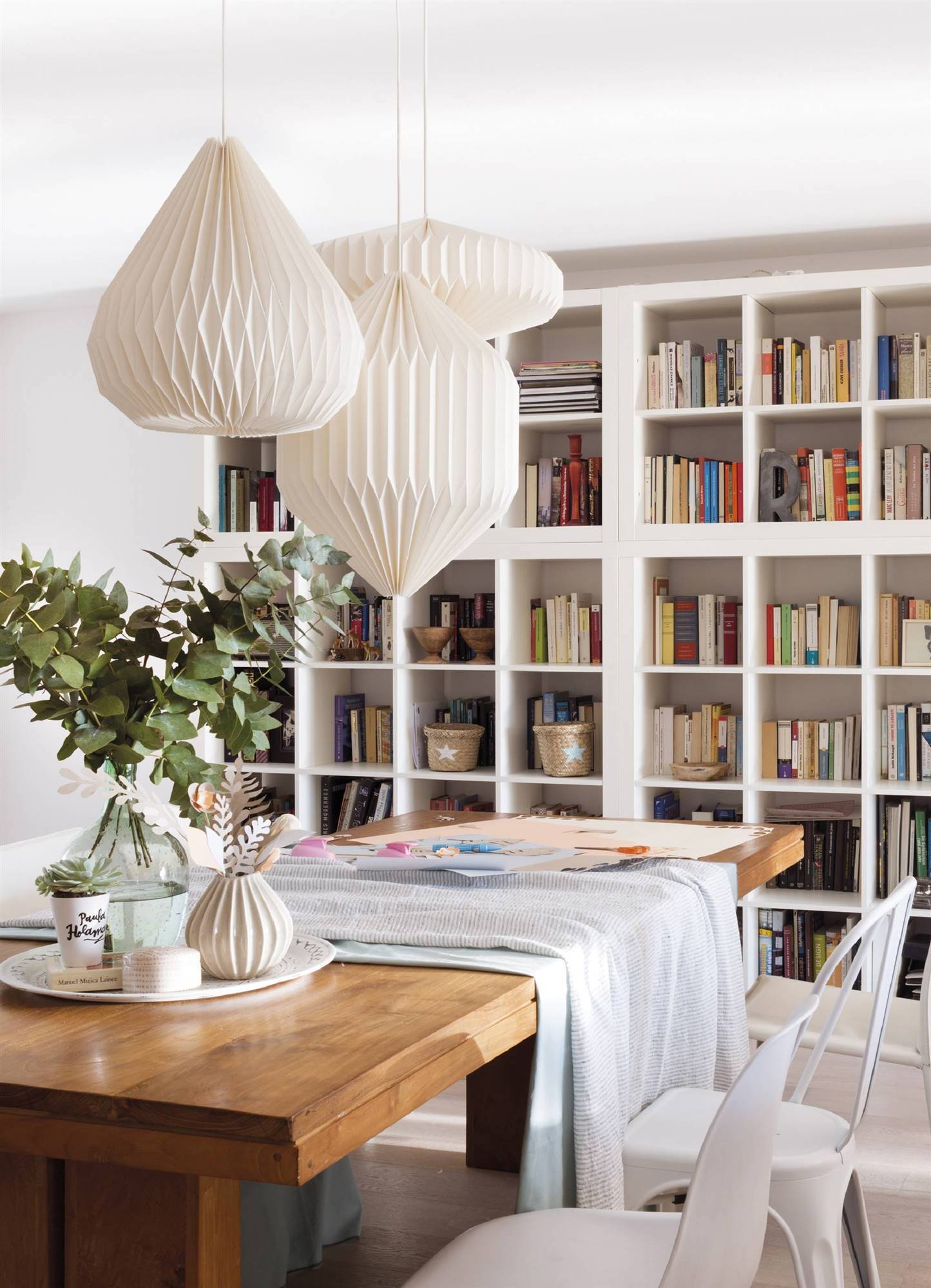 Comedor con mesa de madera, lámparas de techo de papel y librería blanca