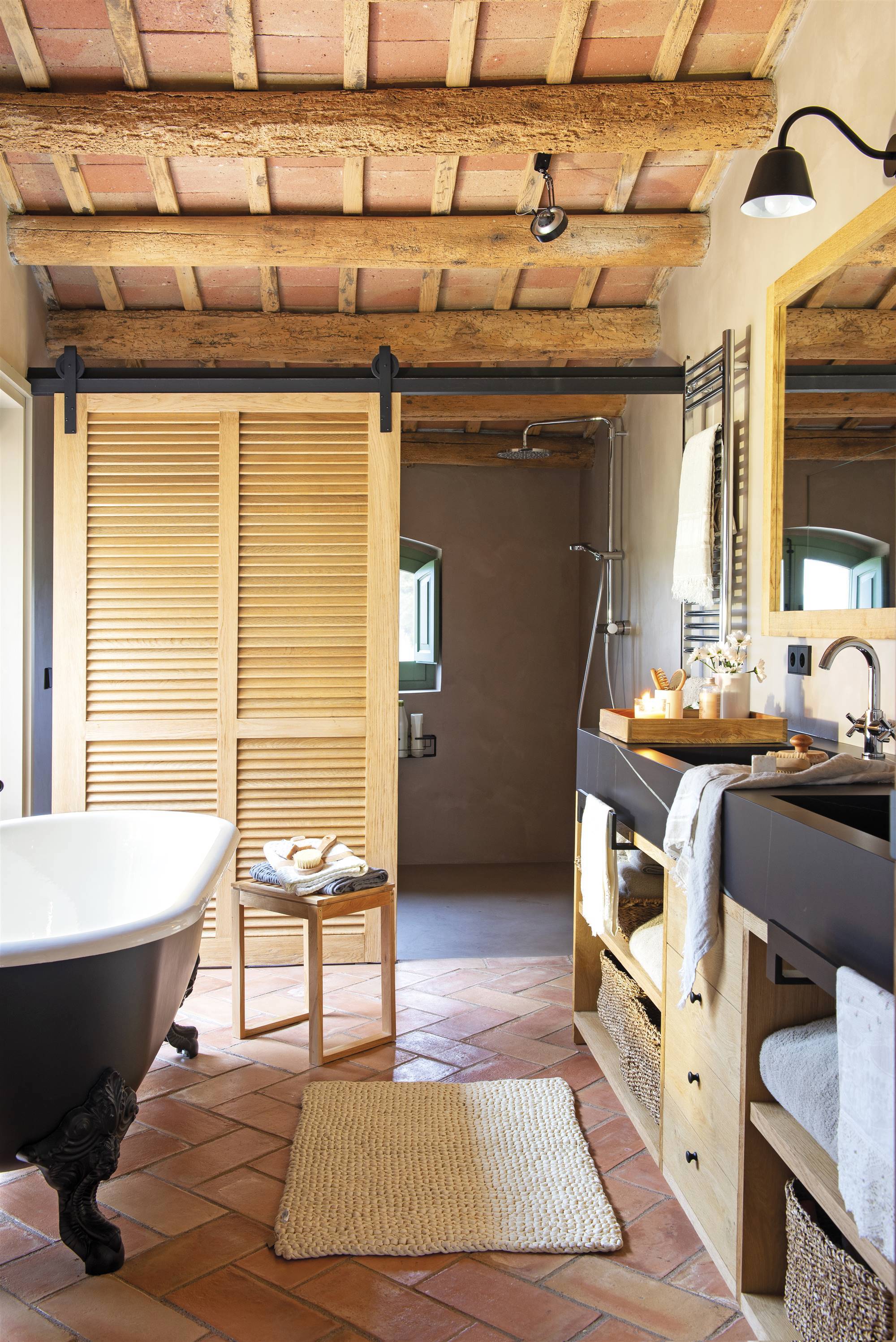 Baño rústico con bañera exenta con patas y ducha separada por una puerta de madera. 
